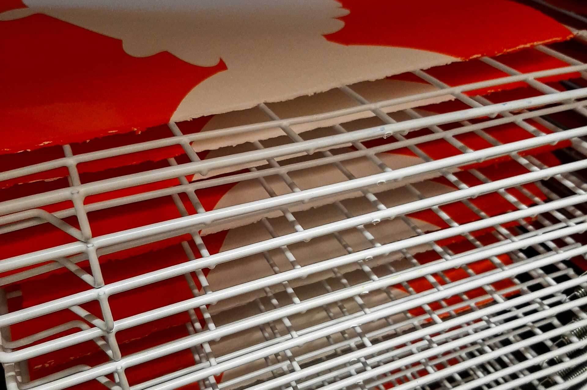 Multiple screen prints drying on a spring‑loaded rack with wire shelves, showing organised drying in a compact studio.