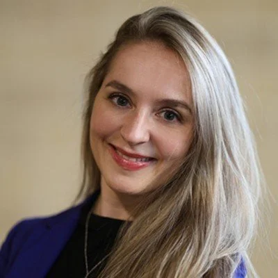 A young woman with long blonde hair smiling at the camera, wearing a blue blazer and black top.