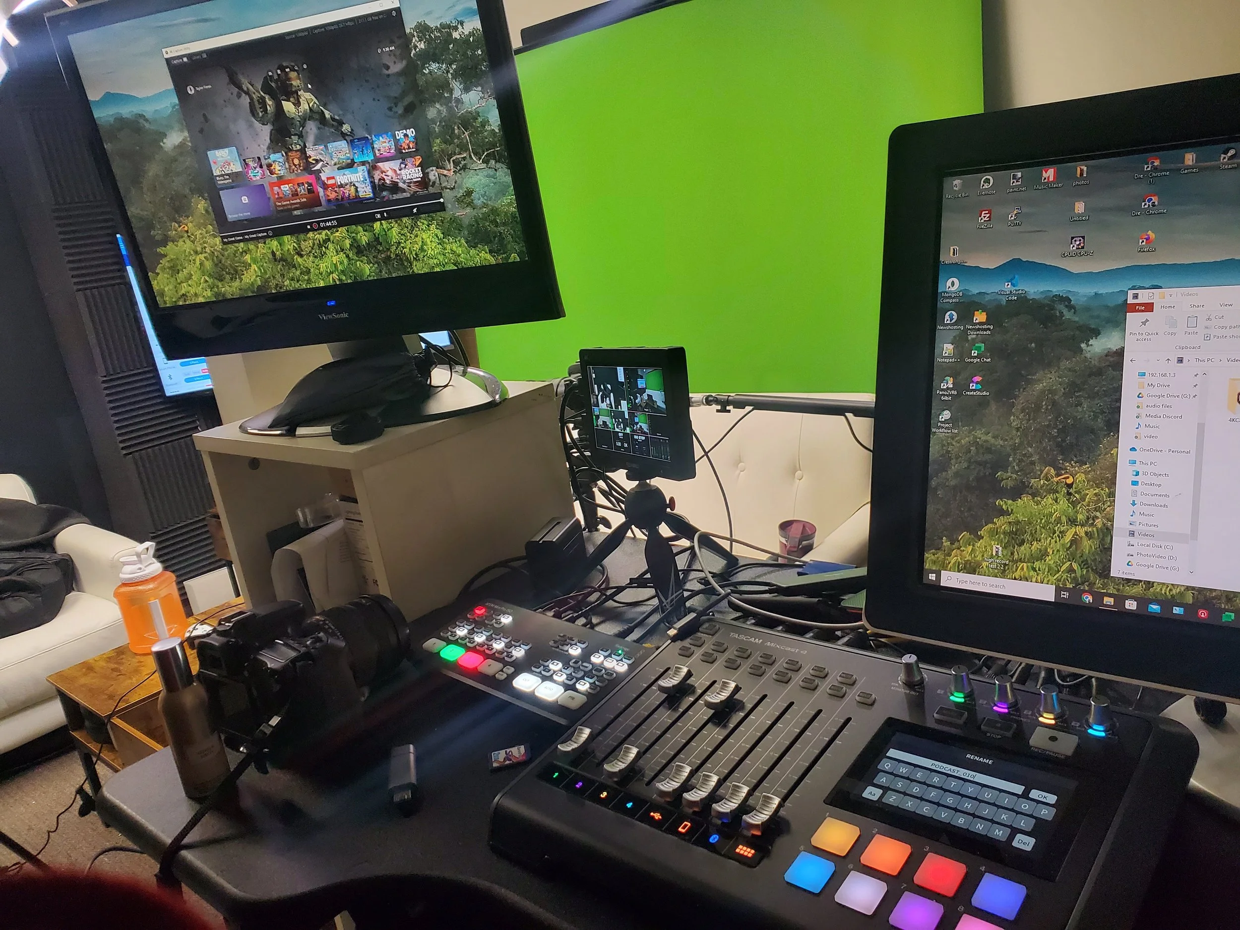 A video editing or streaming setup with multiple monitors, a mixing console, a camera, a small monitor, and various electronic devices on a table.