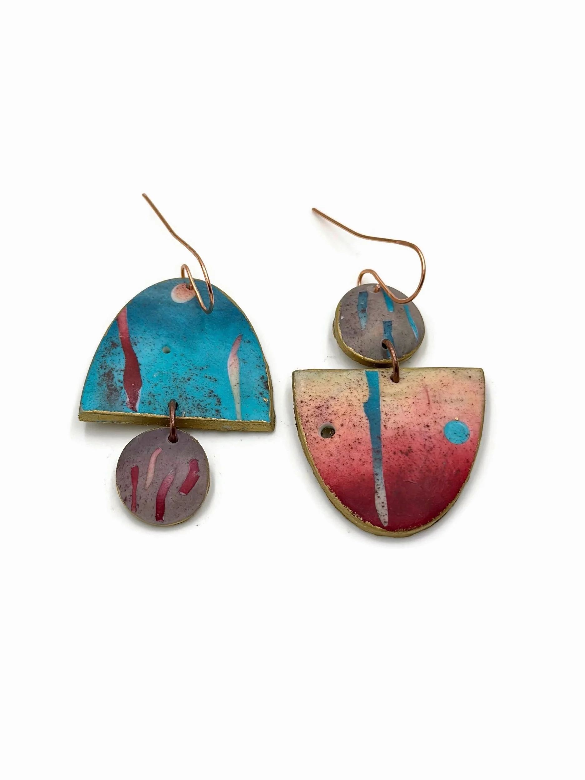 Handmade asymmetrical drop earrings with circular cut-outs in turquoise, muted red, dusty pink, and warm neutral tones.