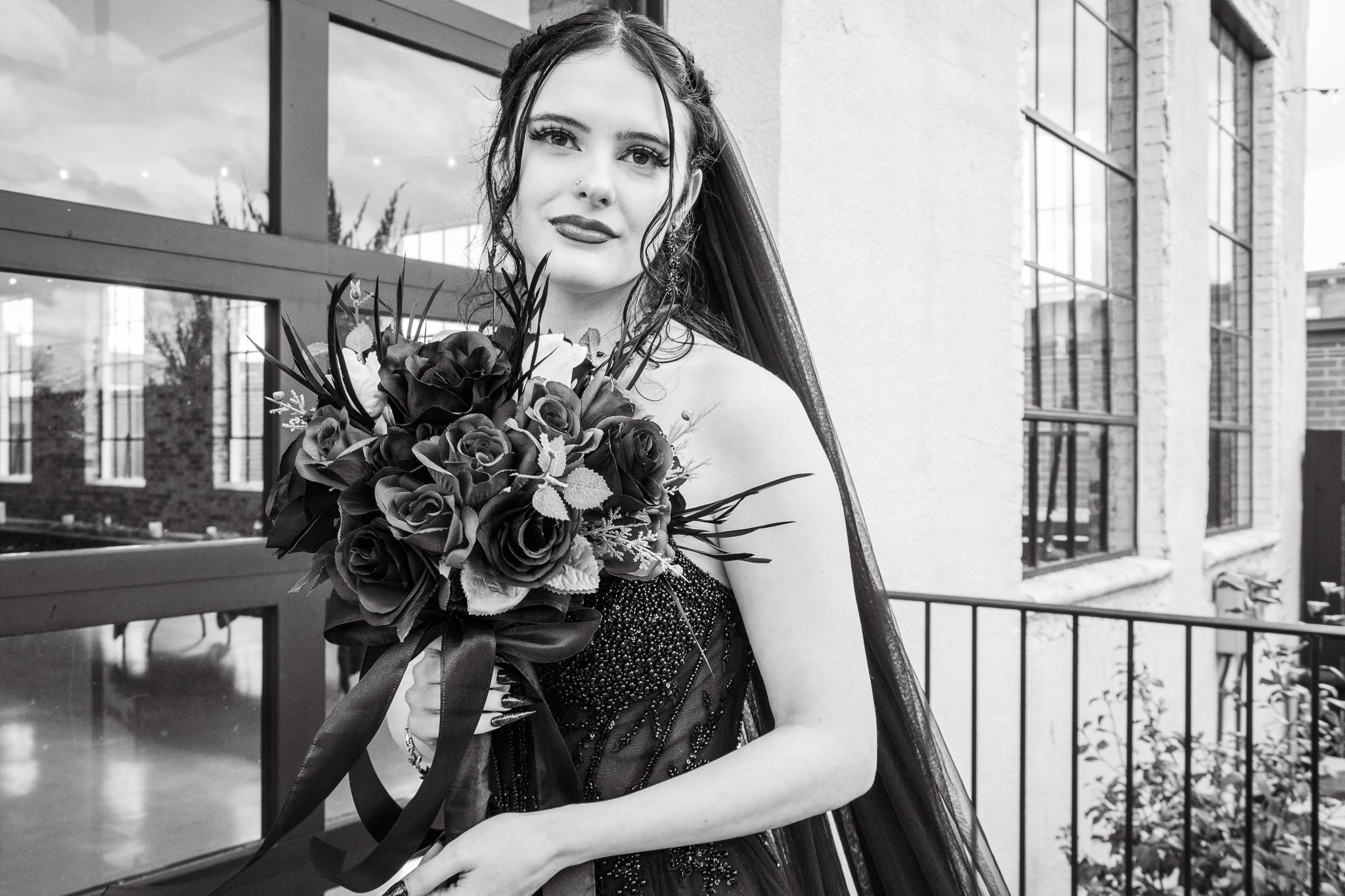 Black and white photo of a woman holding a bouquet of flowers, standing outside near a building with large windows.