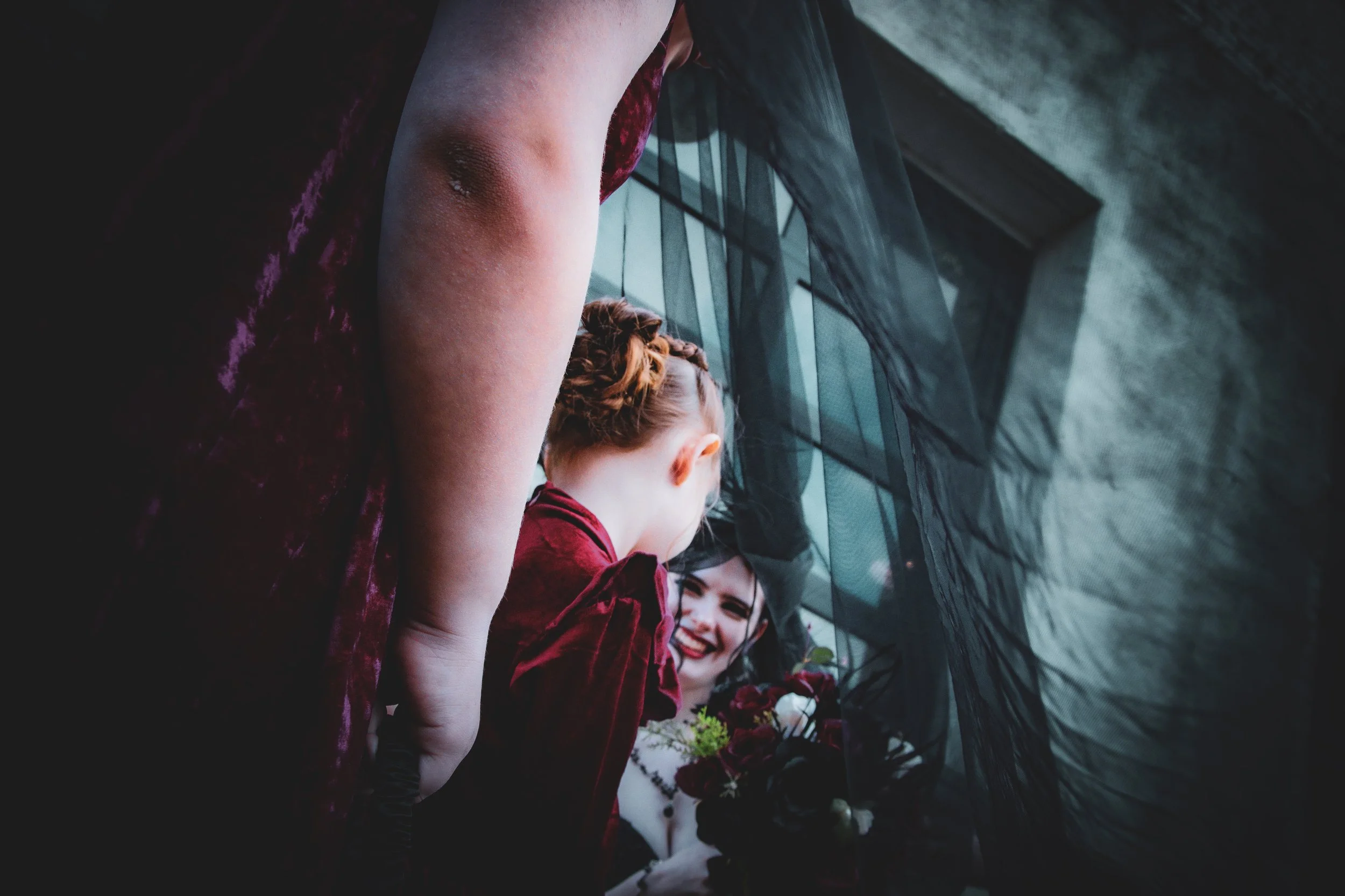 A woman holding a bouquet of flowers, seen through a black sheer curtain, smiling and looking at a person with red hair.
