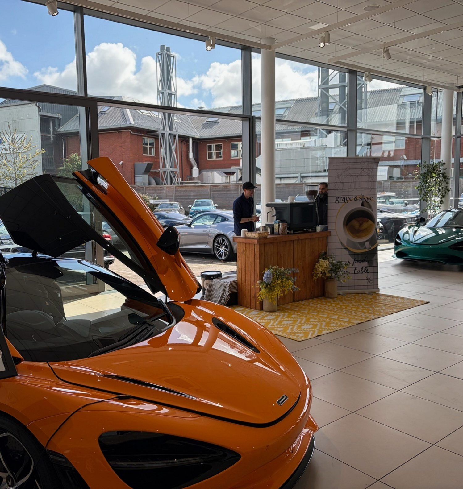 A sports car in a Mclaren garage with the grace&skye coffee bar and a barista standing behind it.