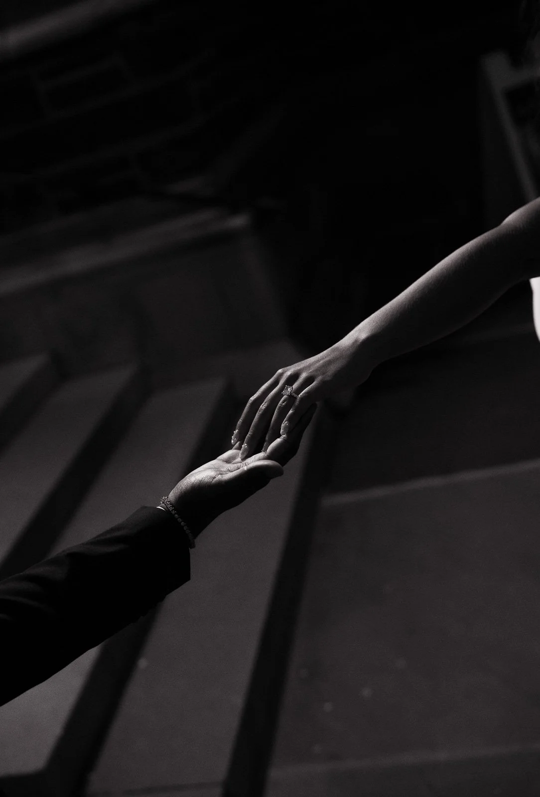 Black and white photo of a man holding his fiance's hand to show off her cushion cut diamond engagement ring at Duke Chapel at Duke University.