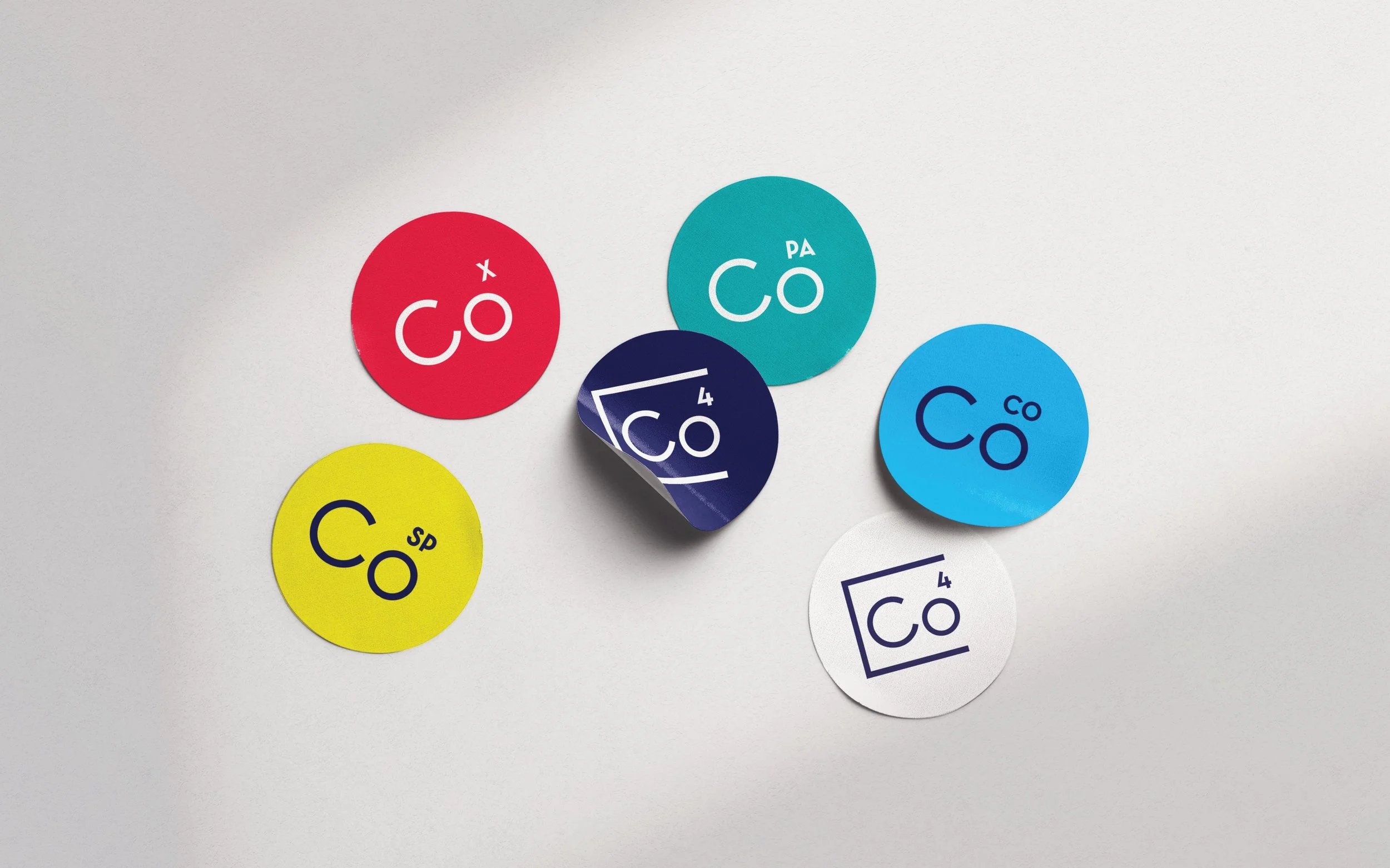 Colorful round stickers with variations of "Co" design on a white surface.