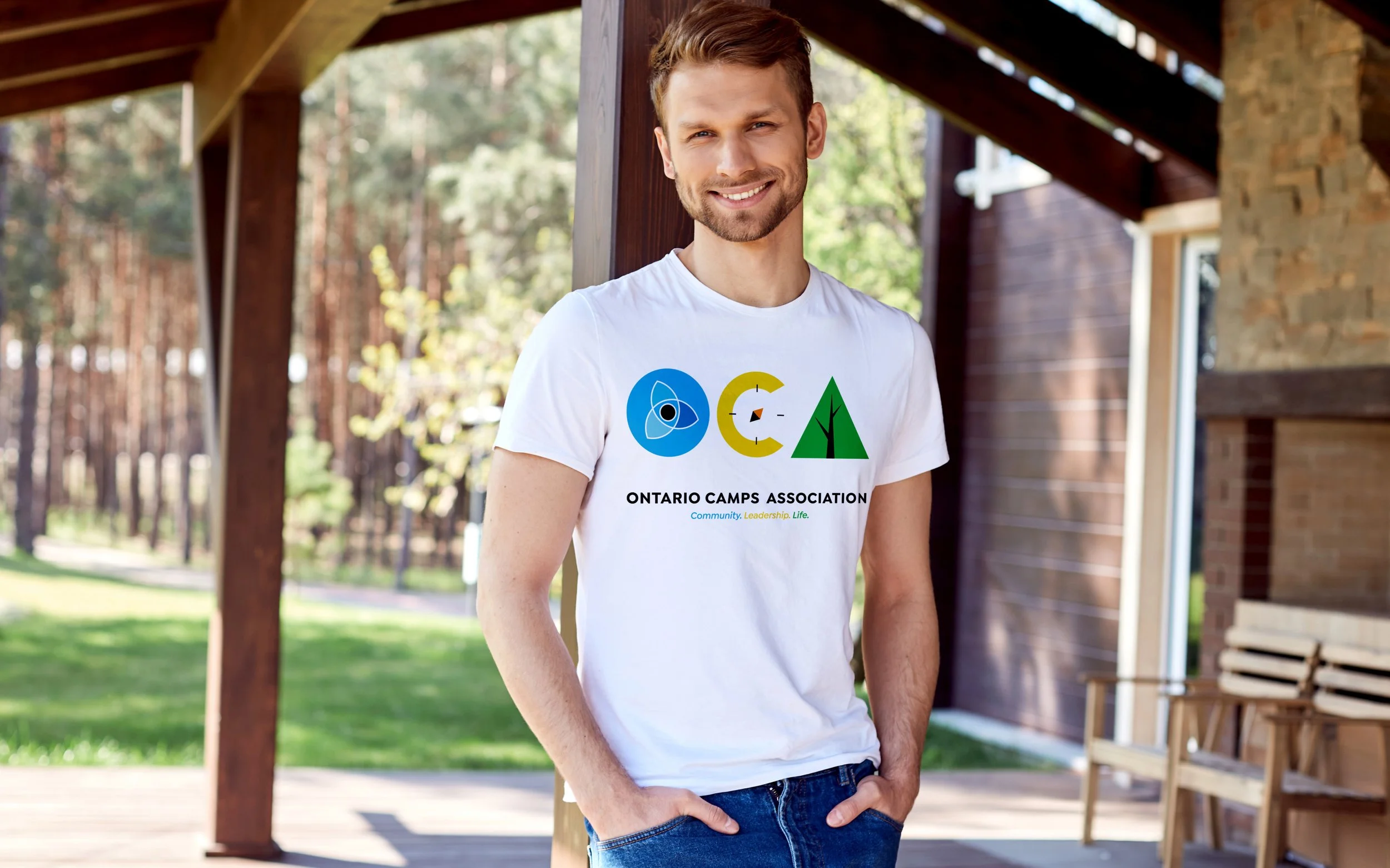 Person wearing an Ontario Camps Association t-shirt on a wooden porch with trees in background.