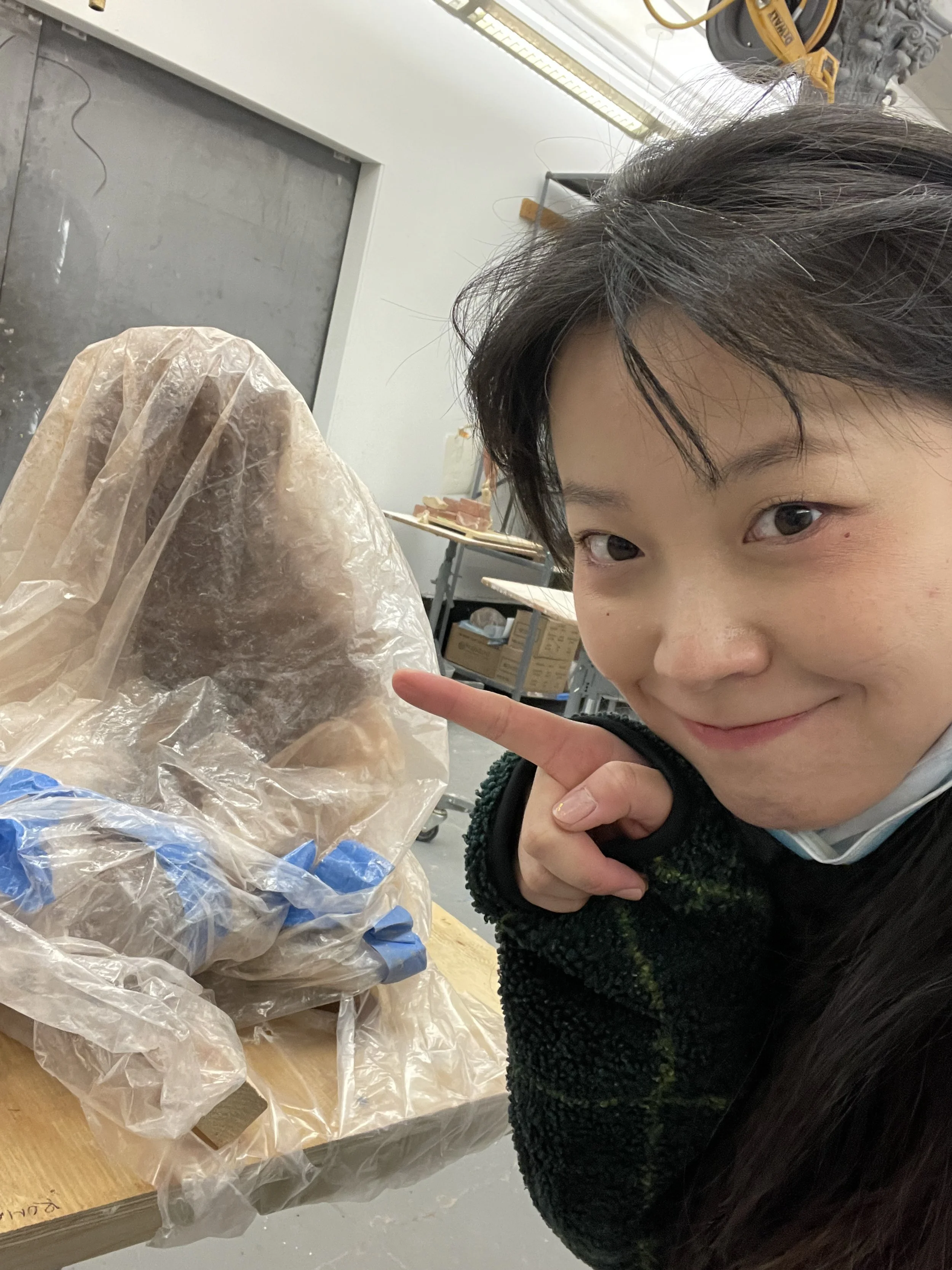 A young person smiling and pointing at a person in a protective suit and mask, with a workshop or laboratory setting in the background.