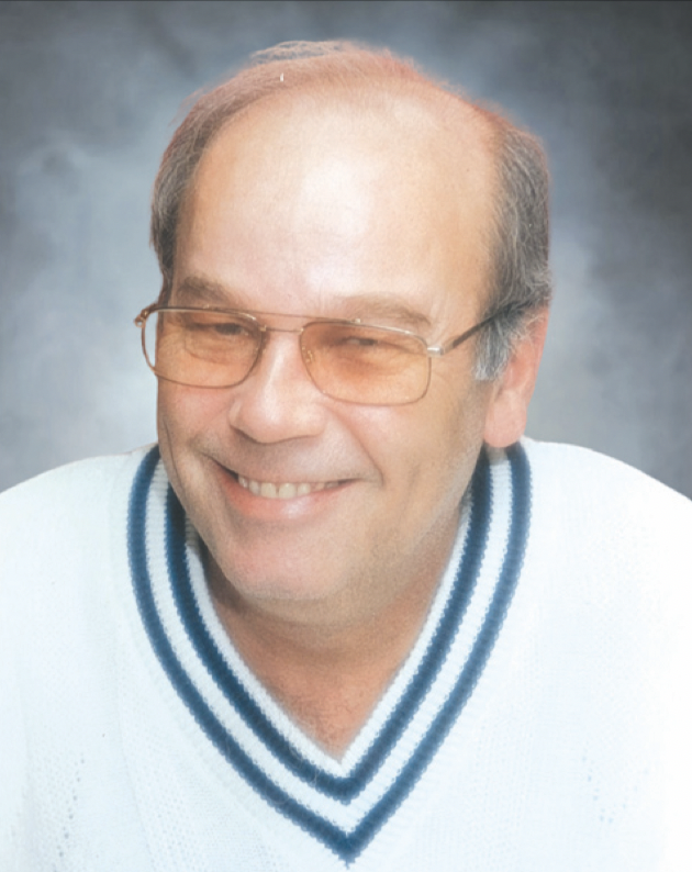 A middle-aged man with glasses, smiling, wearing a white sports jersey with blue and black stripes on the collar.