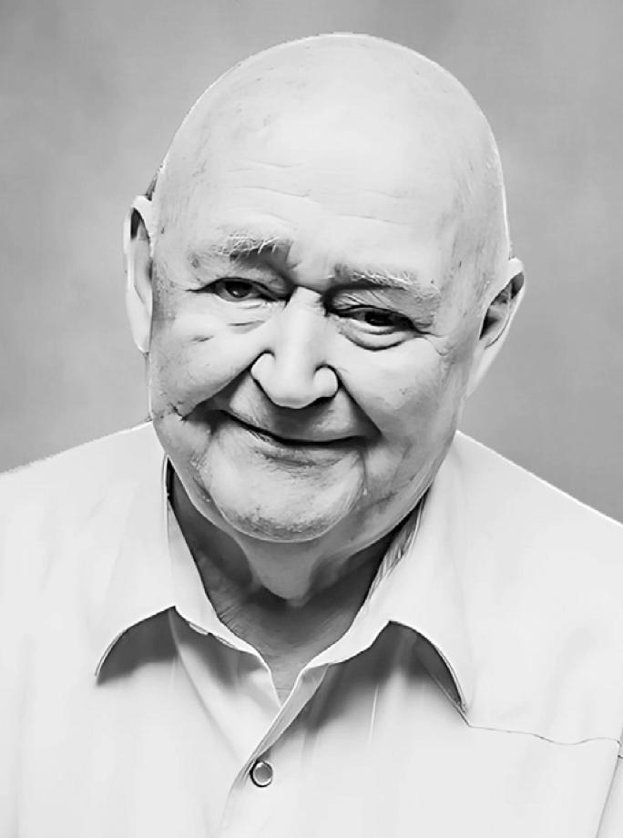 Black and white photo of an elderly man with a bald head, smiling, wearing a collared shirt.