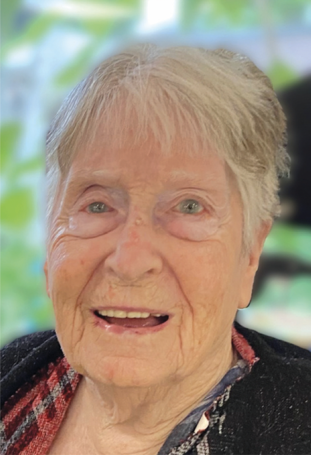 Close-up of an elderly woman with short, light-colored hair smiling at the camera, with a blurred green outdoor background.
