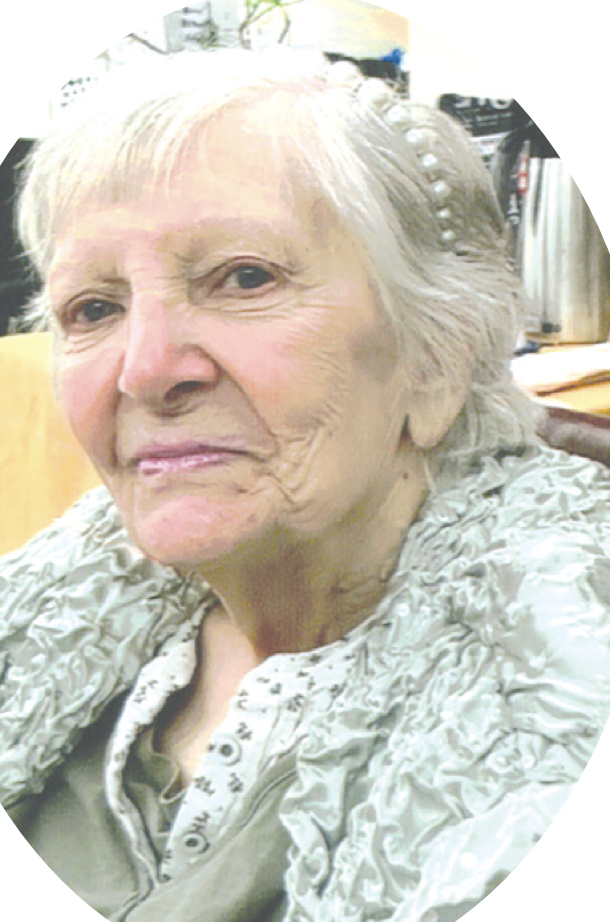 Close-up of an elderly woman with short white hair, wearing a patterned gray and white blouse, in an indoor setting.