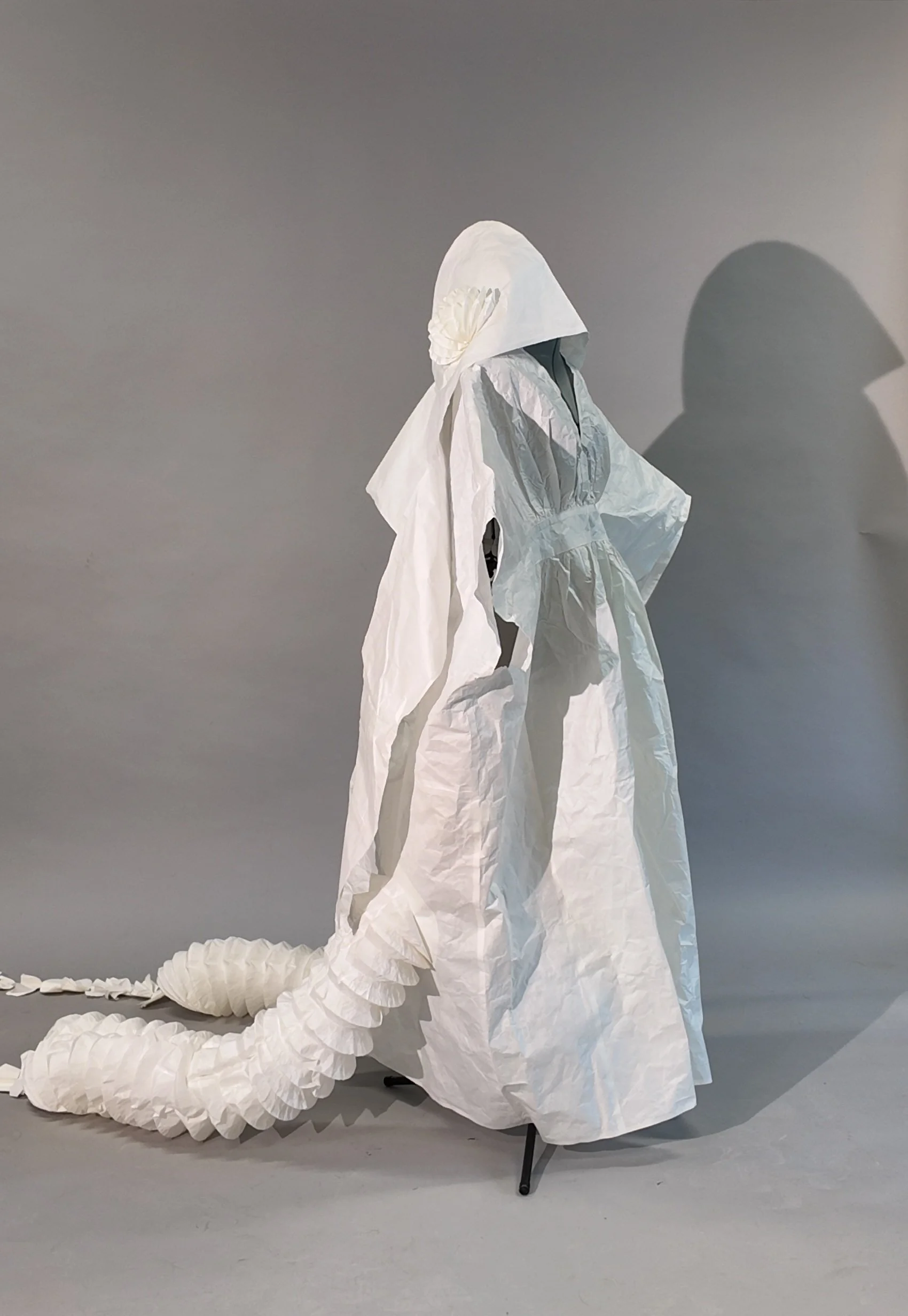 Final version of the squid-yokai costume in white washi paper, showing the straight robe-like silhouette, widened sleeves, and two extended pleated tentacles. Photograph by Yuting Zhou, 2026.