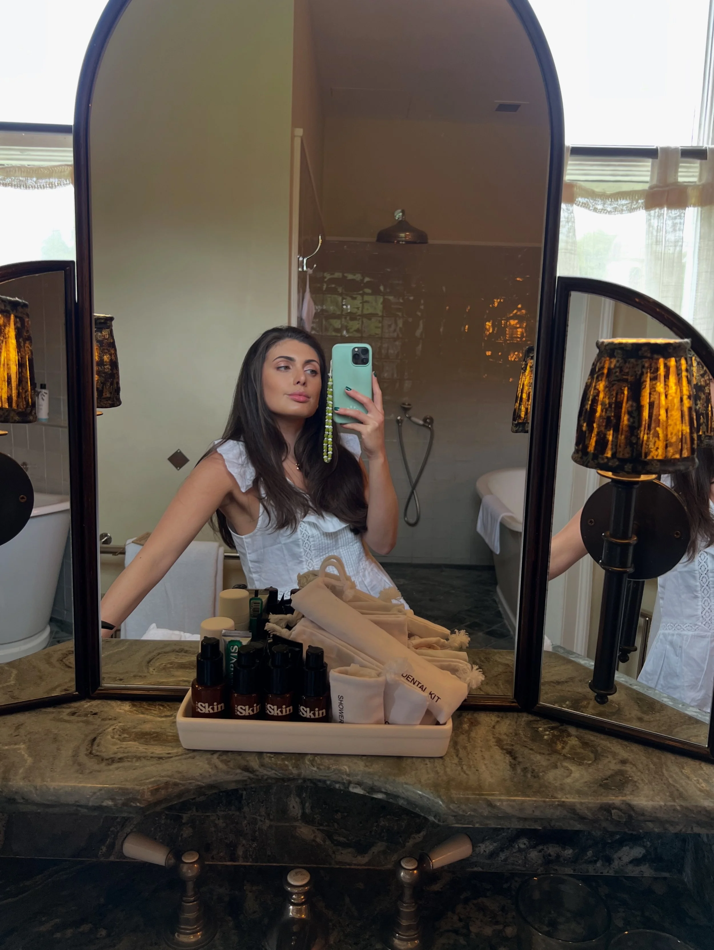 A woman taking a selfie in a bathroom mirror with her phone, showing the by saffron beaded phone charm accessory.