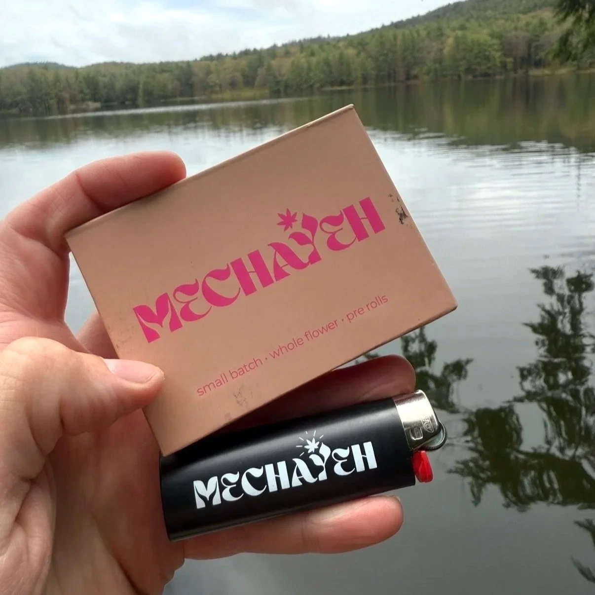 Mechayeh variety pack box and Mechayeh lighter held up in front of a Vermont lake