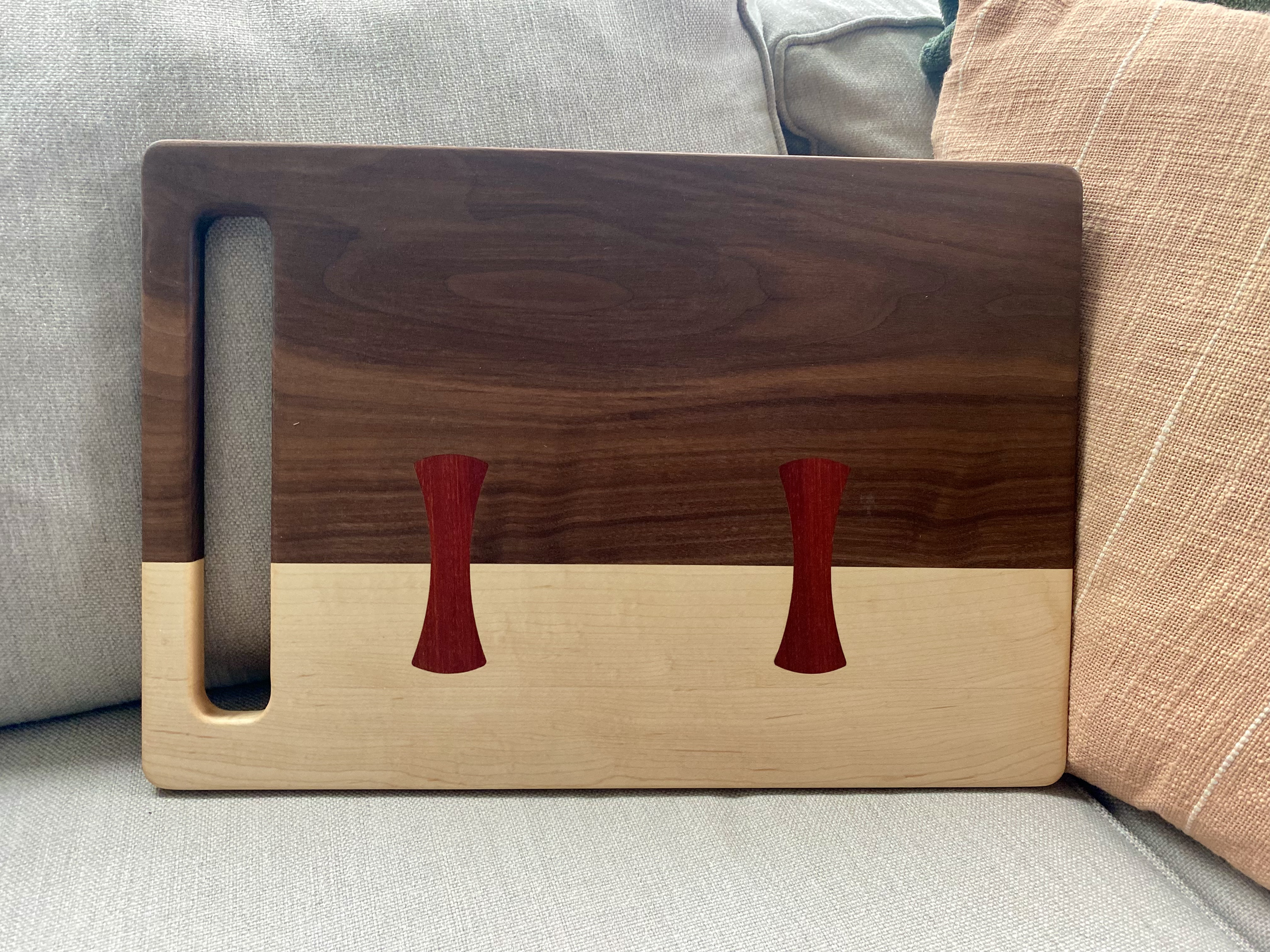 Walnut and maple cutting board with bloodwood bow-tie inlays and integrated handle, designed for chopping, slicing, food prep, and serving.