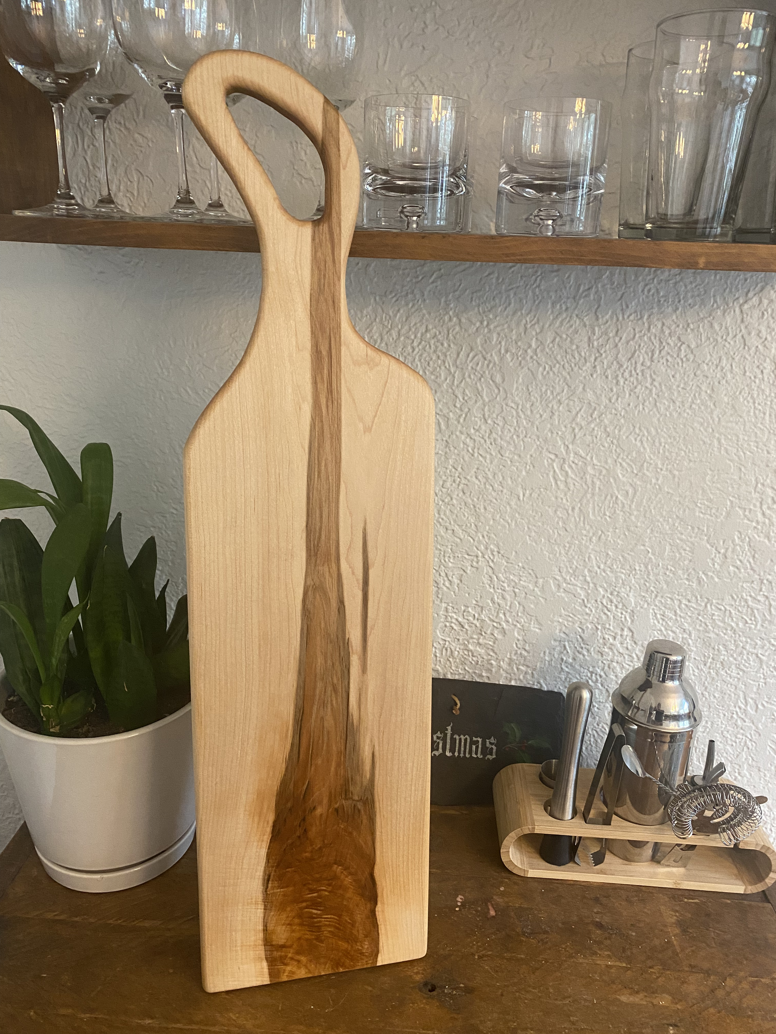 The Maple Monolith, a large one-piece maple charcuterie board with handle, featuring dramatic natural grain and smooth hardwood surface for serving.