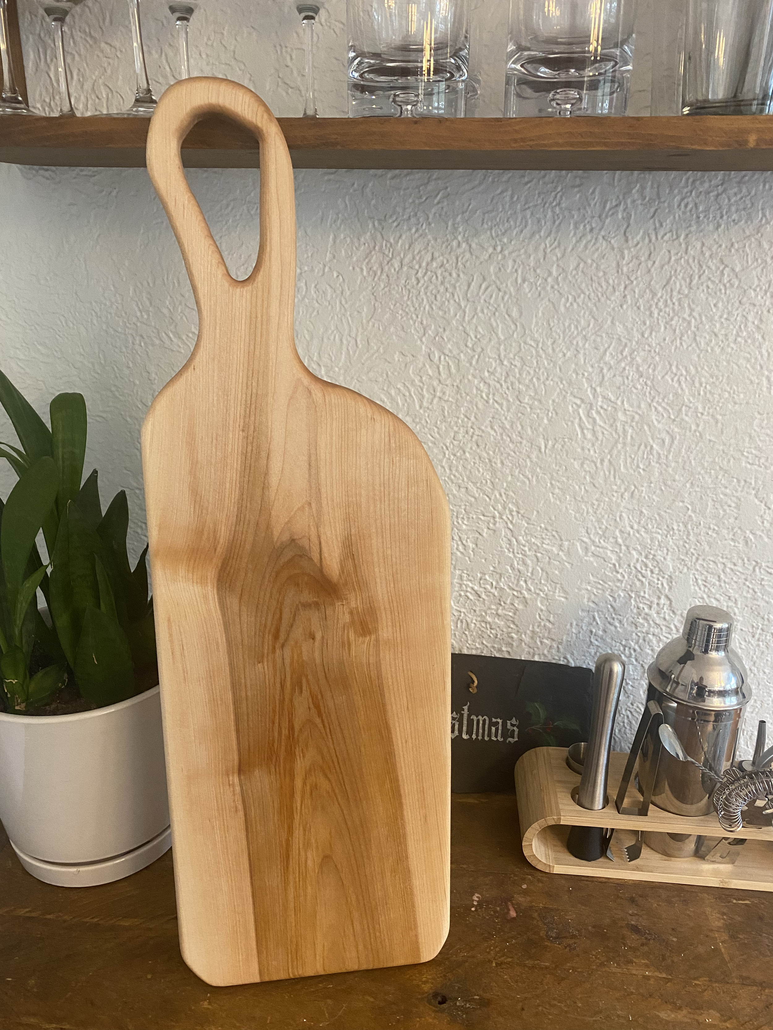 The Hearth Board, a large one-piece maple charcuterie board with handle, featuring natural color variation and smooth hardwood surface for serving cheese and meats.