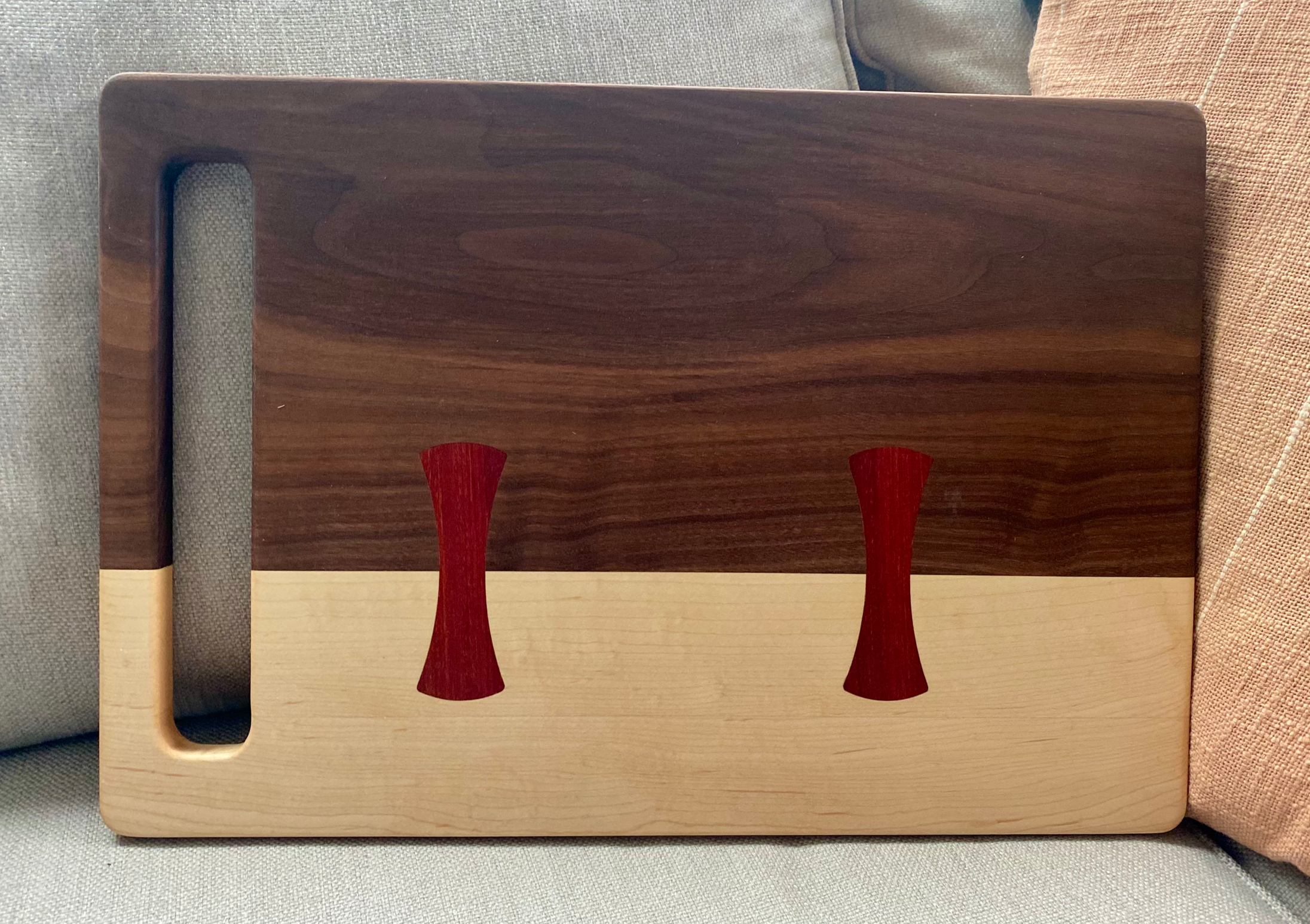 Walnut and maple cutting board with bloodwood bow-tie inlays and integrated handle, designed for chopping, slicing, food prep, and serving.