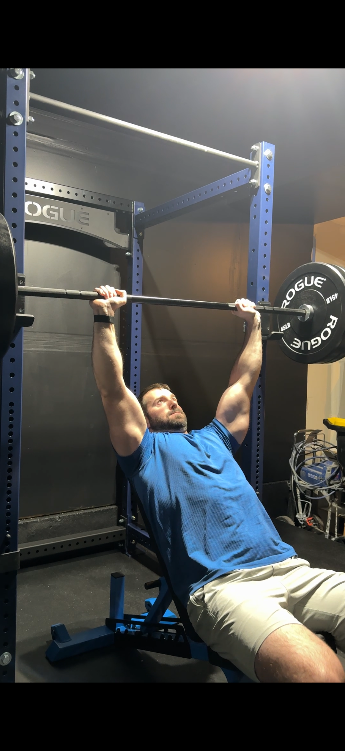 Man lifting a barbell with weights while seated on a workout bench in a gym.