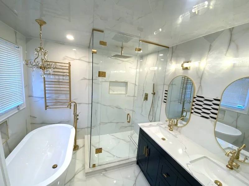 Frameless glass shower with full-height white porcelain tile walls, rainfall showerhead, and antique gold fixtures in a custom Ensuite Master bathroom remodel.