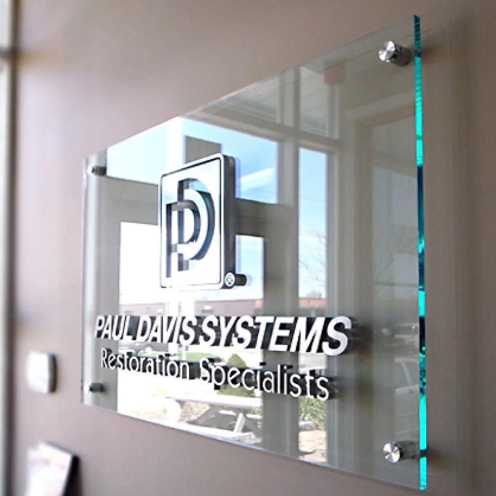Image of a clear acrylic sign installed on a wall with standoffs and 3D LOGO and 3D Letters on top off the clear acrylic representing the business branding.