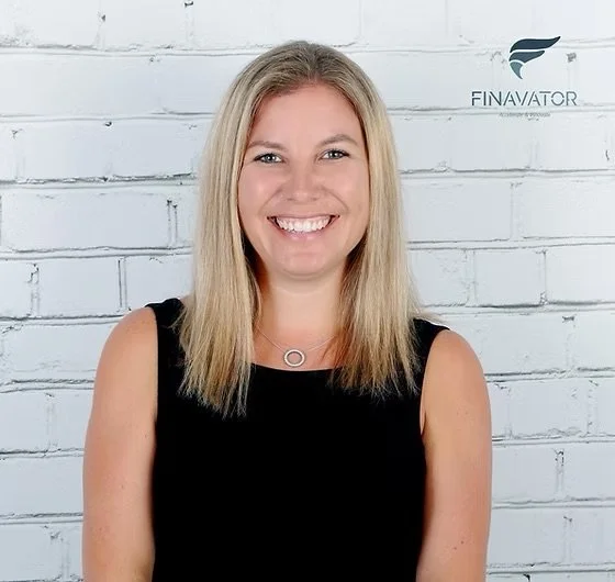 A smiling young woman with blonde hair, wearing a black sleeveless top, standing in front of a white brick wall with a Finavator logo.
