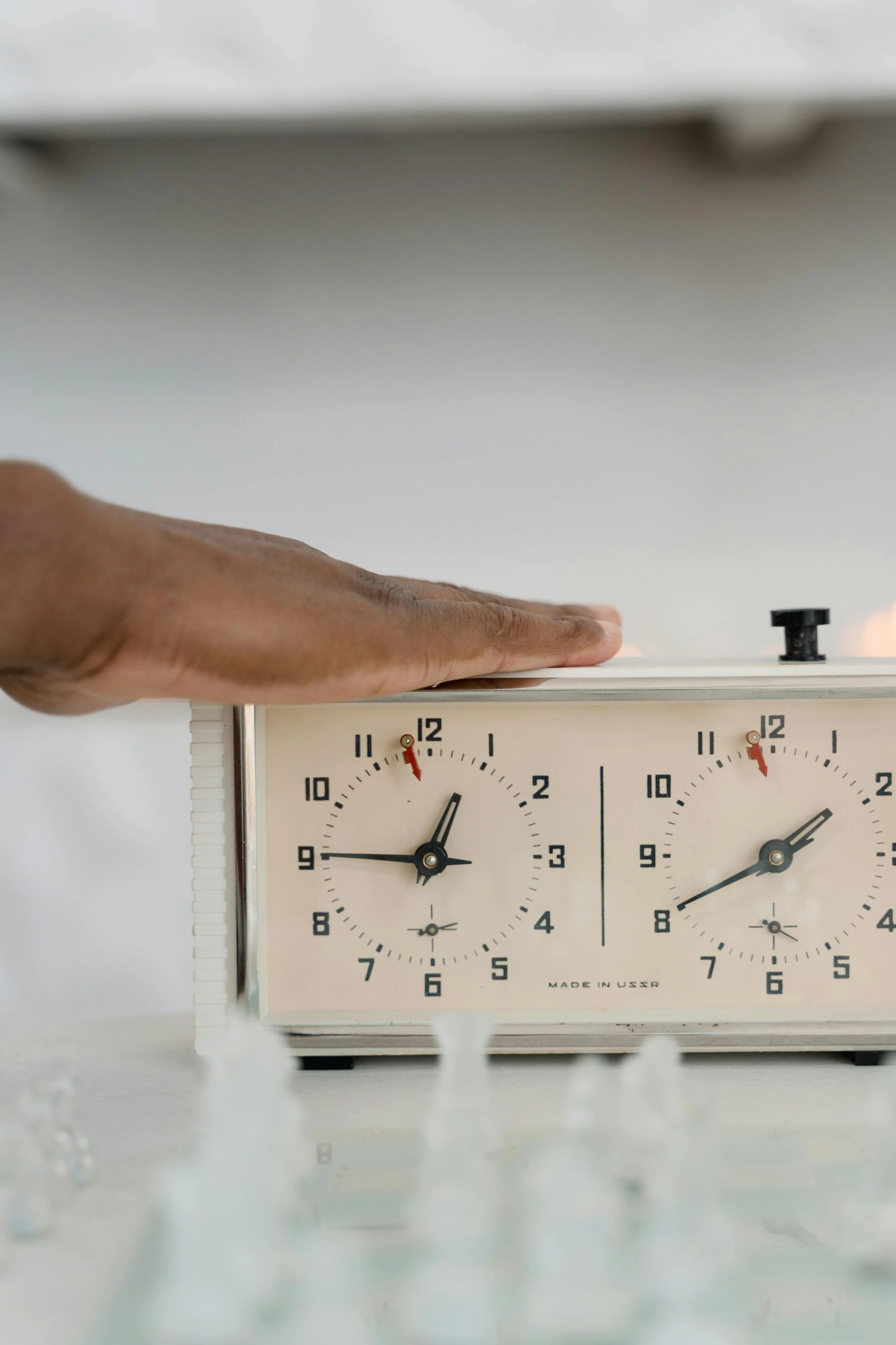 A person pressing down on the top of a chess clock with their hand, showing the time set to around 11:55 on both clocks.
