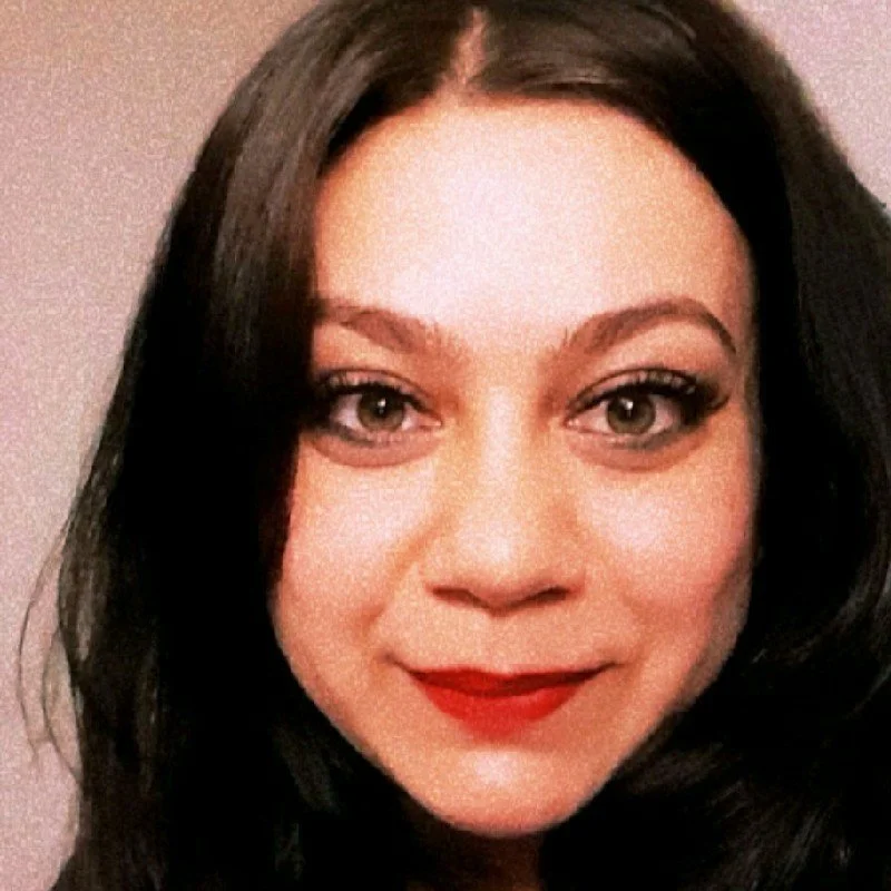 Close-up photo of a woman with dark hair, red lipstick, and makeup, smiling at the camera.
