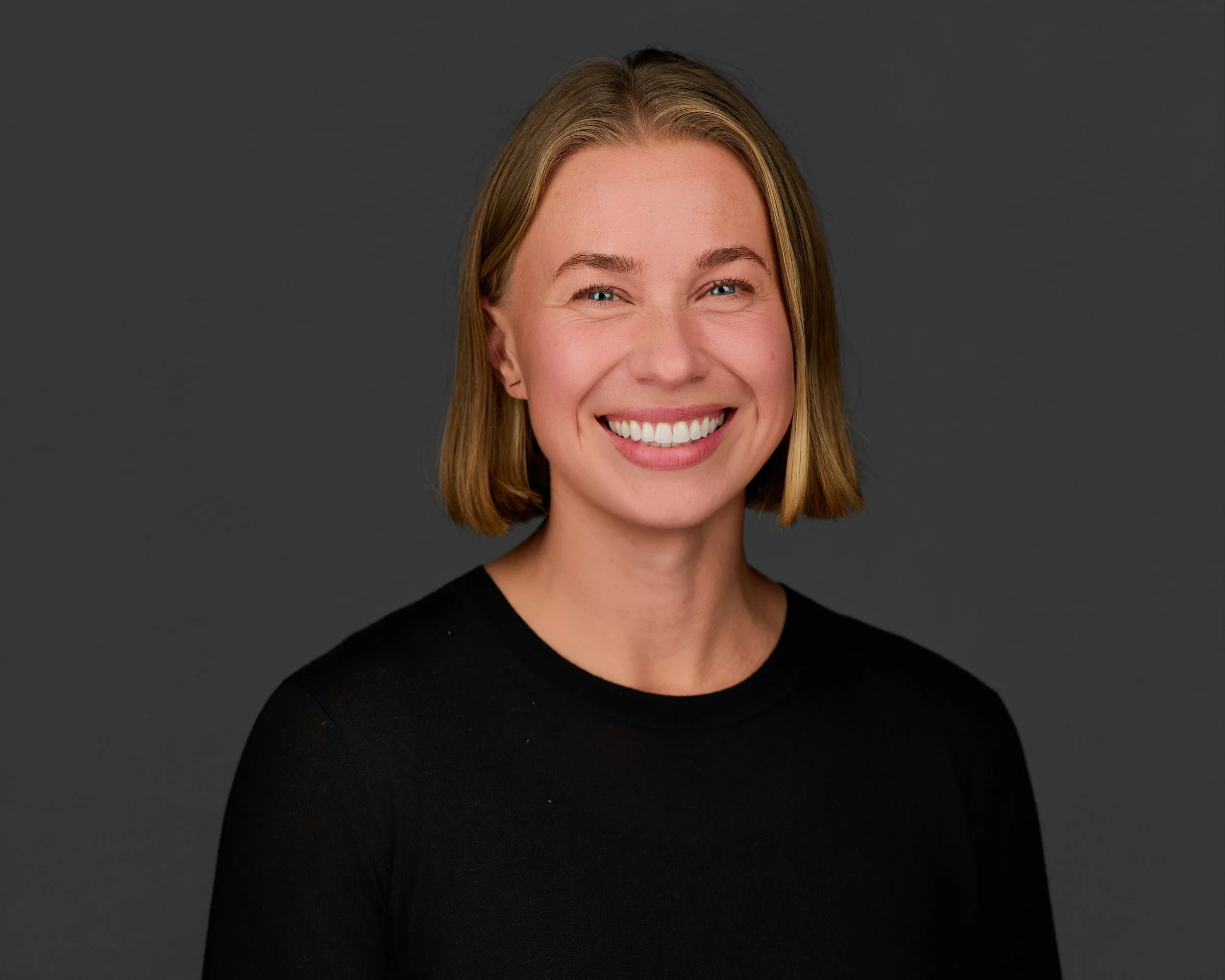 Professional headshot of Brit McKenna, a woman with short blonde hair and blue eyes, smiling broadly against a neutral gray background.
