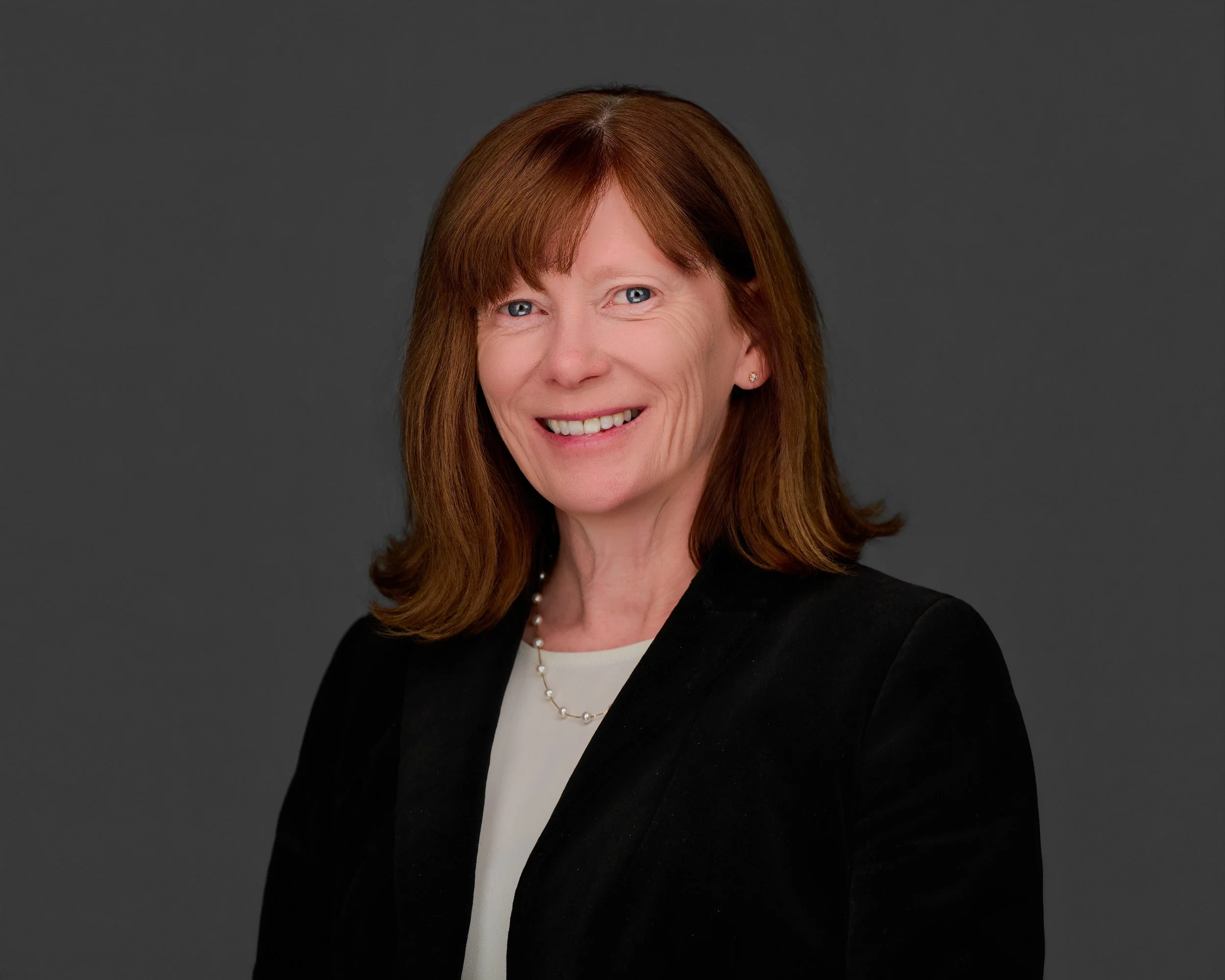 Professional headshot of Donna Curtain, a woman with shoulder-length auburn hair and blue eyes, smiling warmly against a neutral gray background.