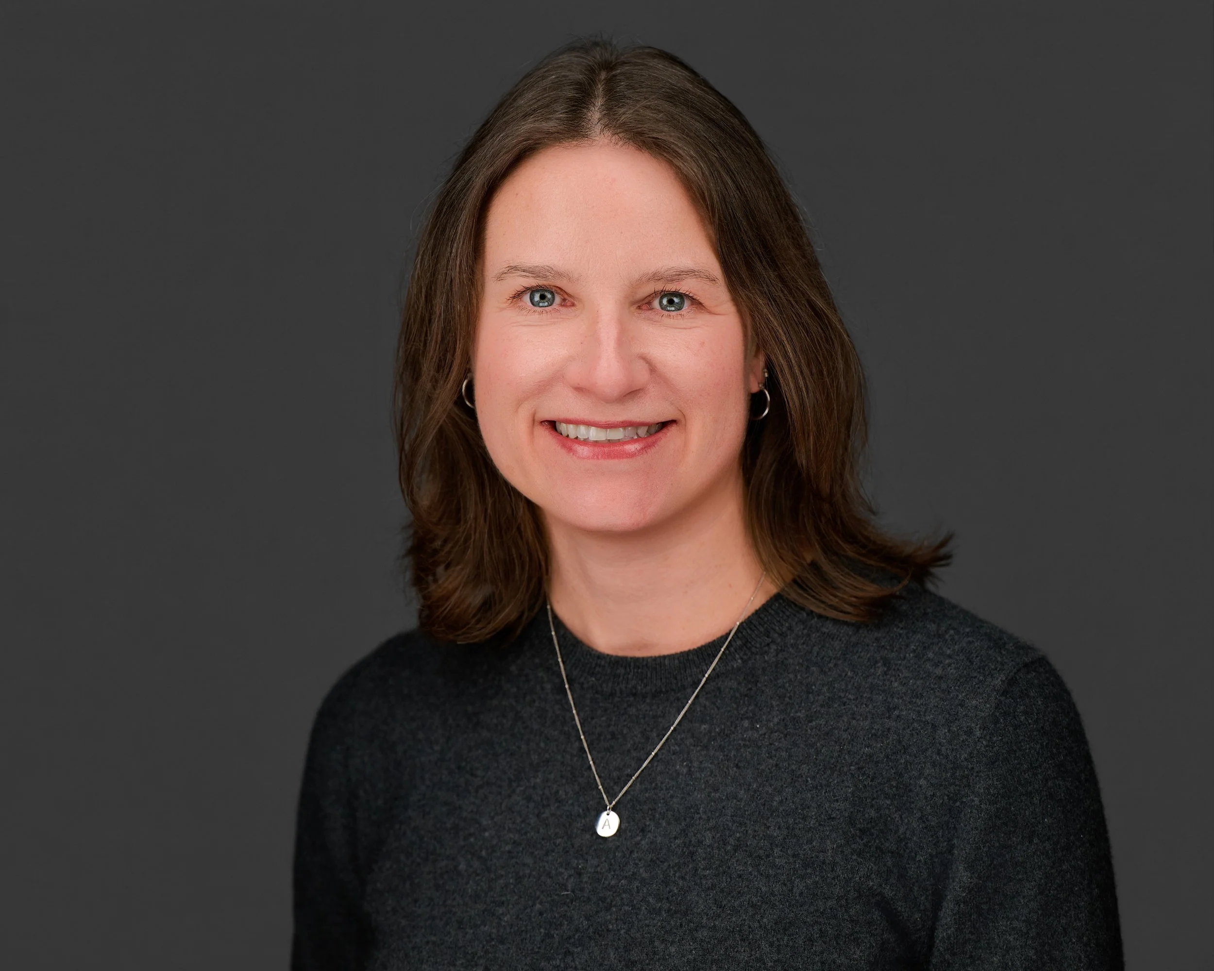 Professional headshot of Abryana Wood, a woman with shoulder-length brown hair and blue eyes, smiling warmly against a neutral gray background.