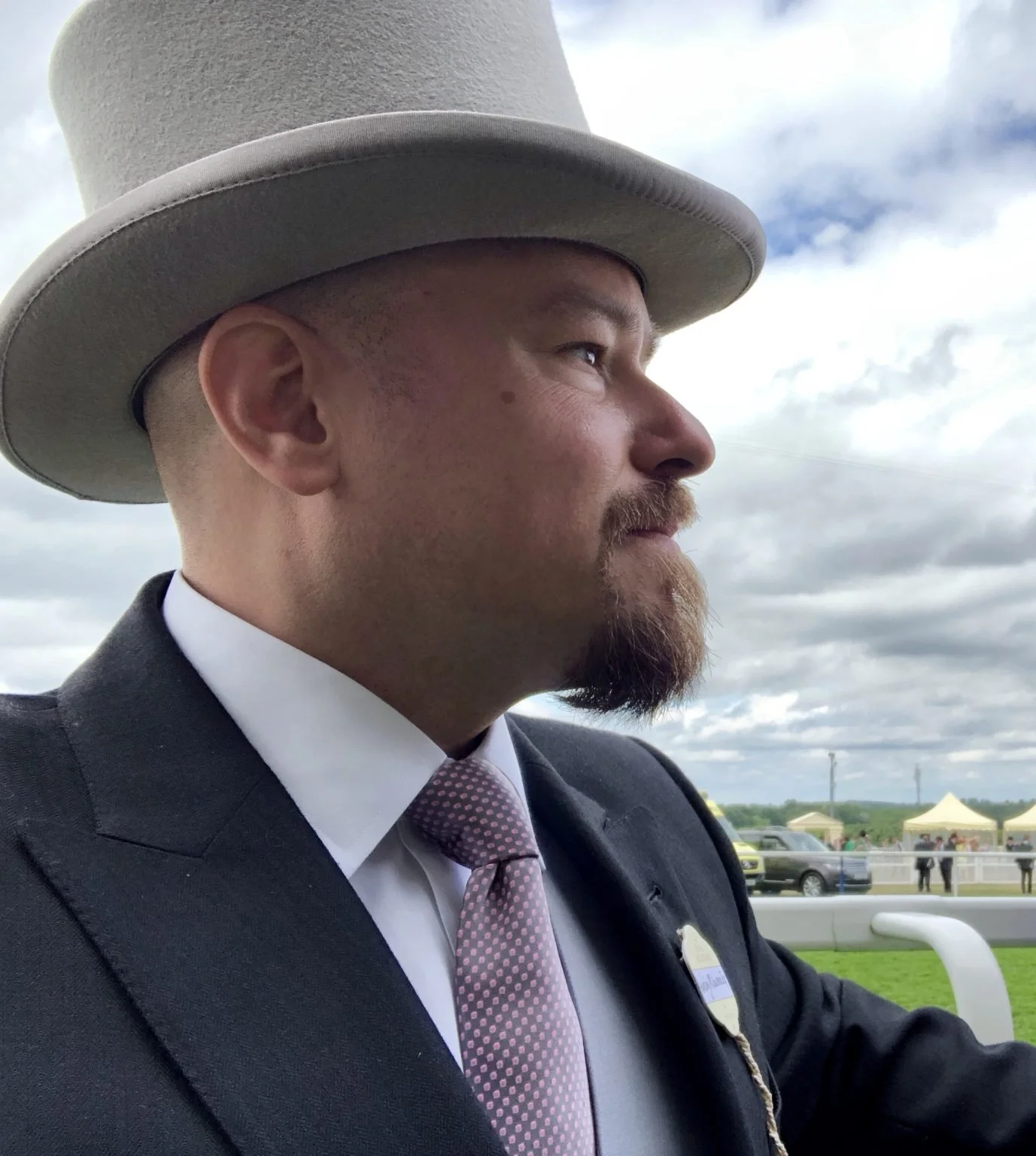 Professional photo of Wesley Lawrence, a man with a beard wearing a suit, tie, and light gray hat, photographed in profile outdoors against a cloudy sky.