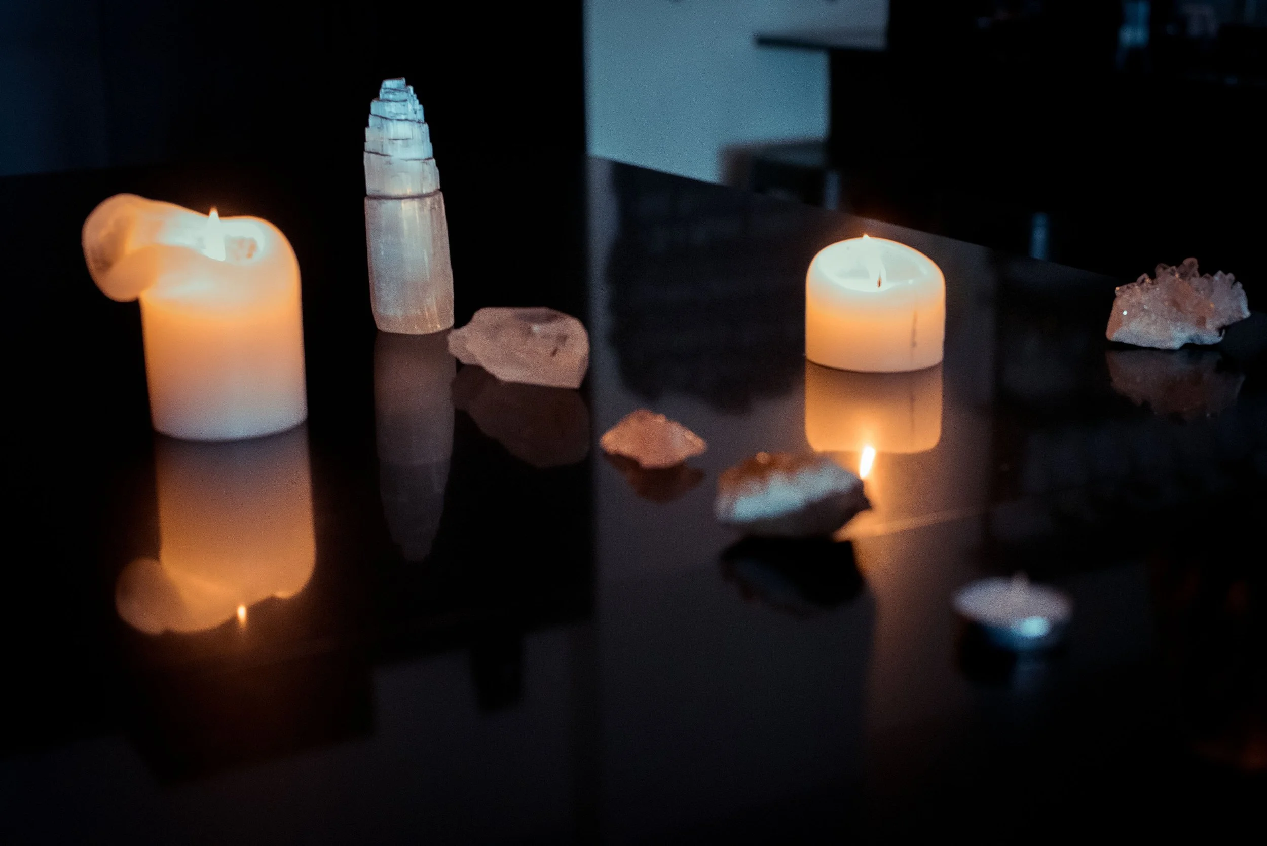 Candles and crystals on a dark reflective surface in a dimly lit room.