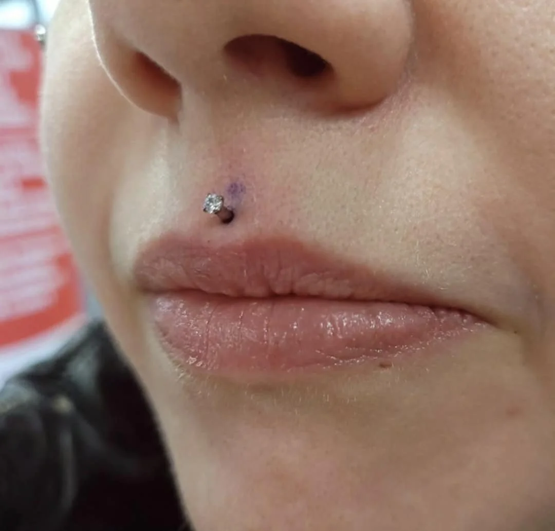 Close-up of a facial piercing above the upper lip with a small diamond-like stud.