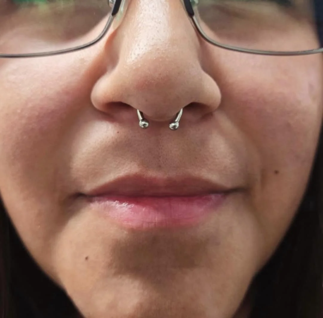 Close-up of a person wearing glasses with a septum piercing.