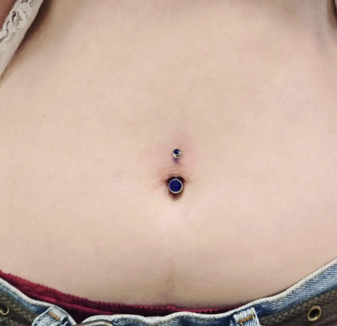 Close-up of a person's belly button with a blue navel piercing.