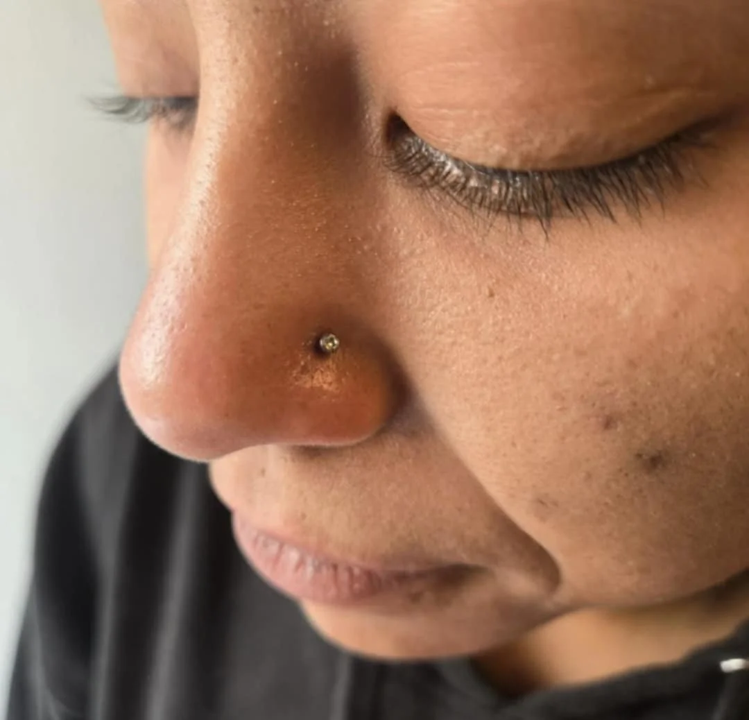 Close-up of a person with a nose piercing and closed eyes.