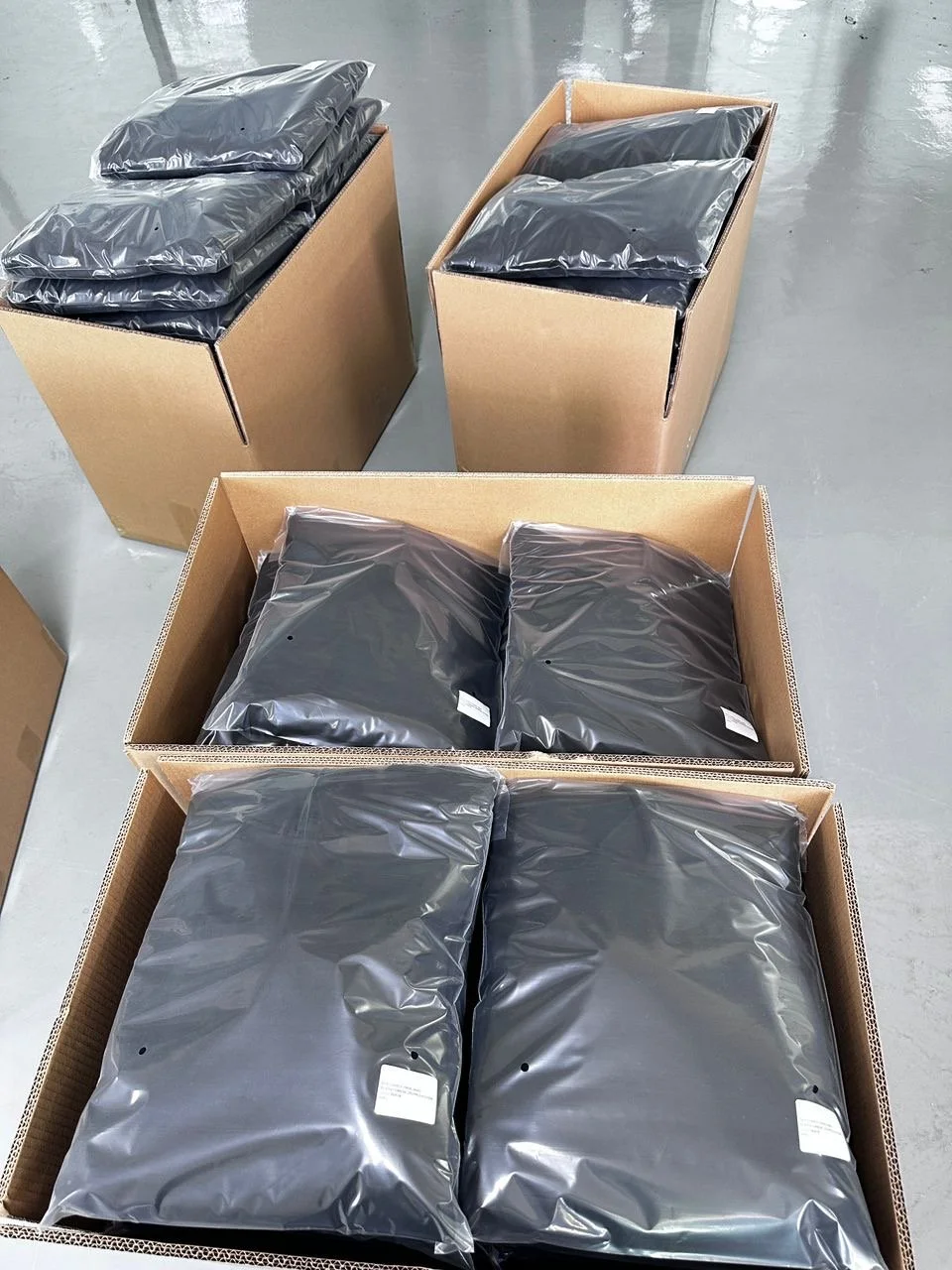 Multiple sealed black packages in open cardboard boxes, likely in a warehouse or storage facility.