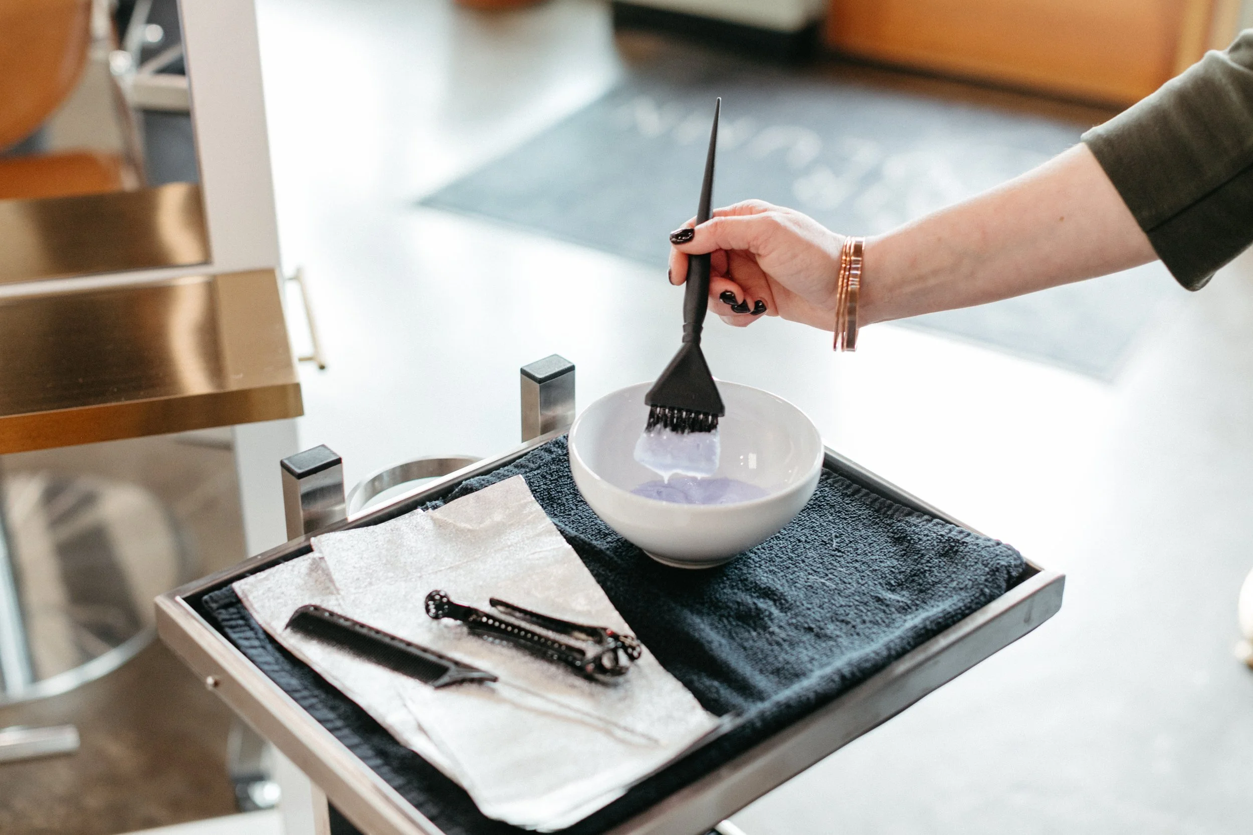 A person setting up with color hair tools in a white bowl at a salon station.