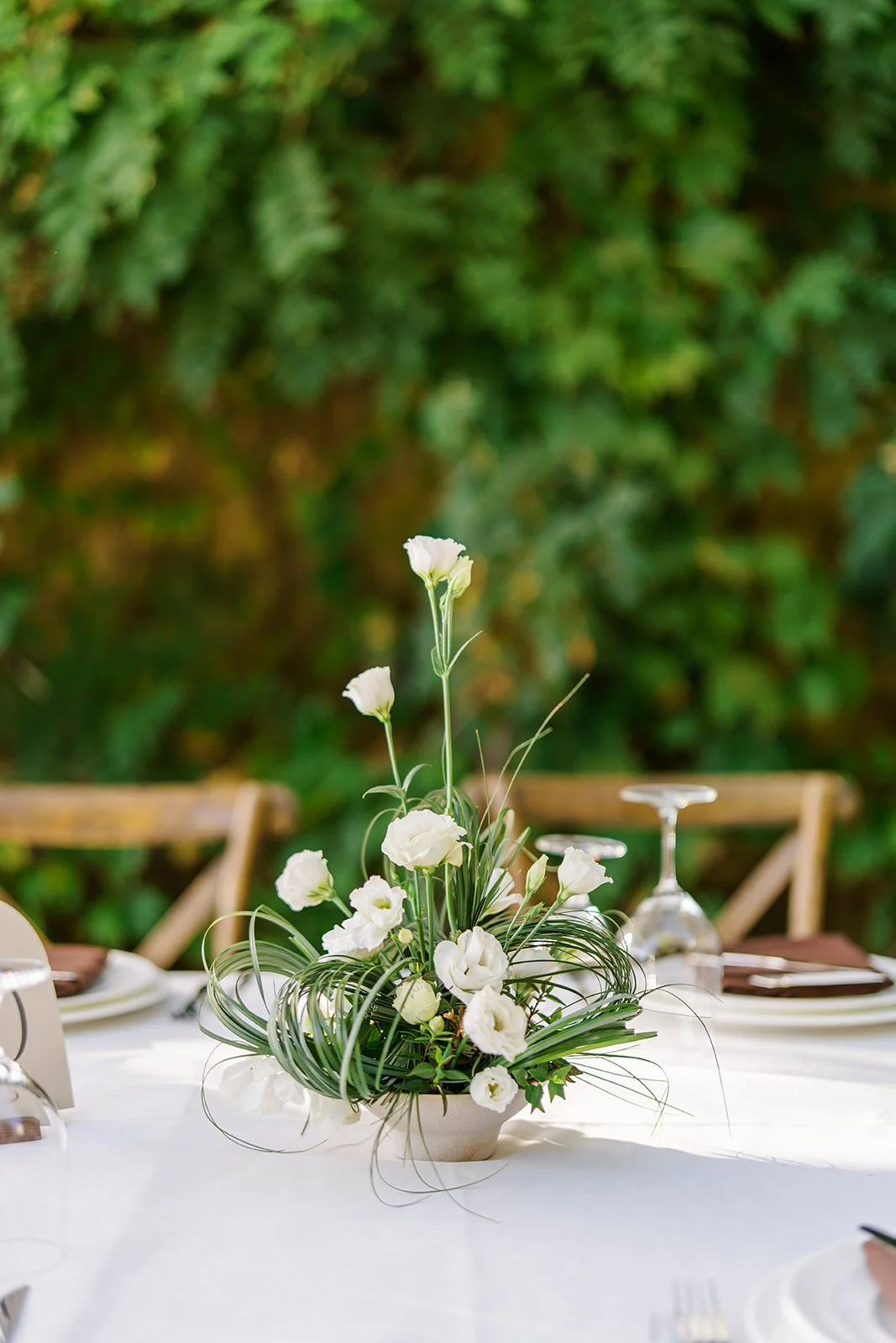 White floral centerpiece with greenery on an outdoor dining table