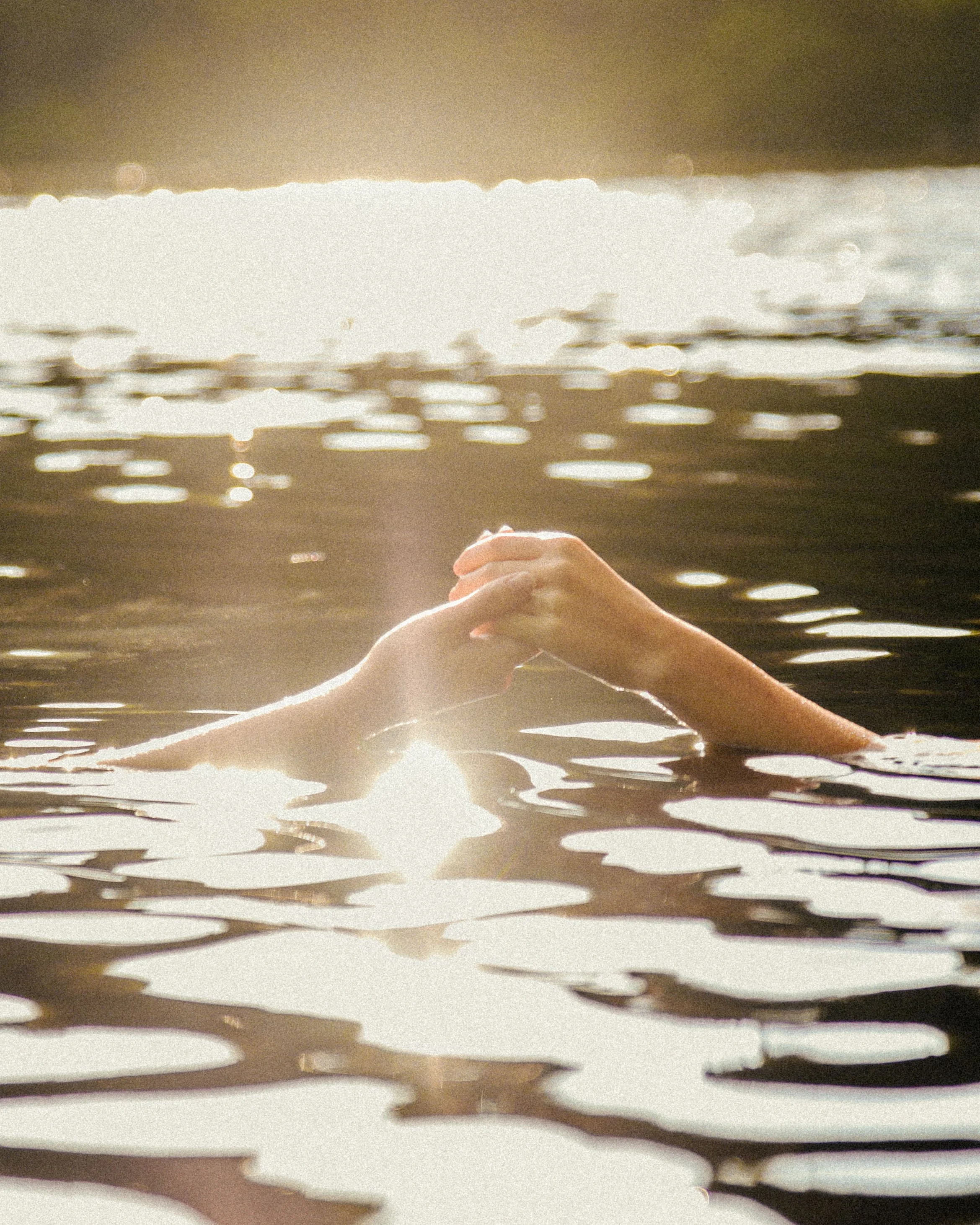 Close-up of a person, mostly the arm and hand, reaching into or through a reflective, metallic, and textured surface with light shining against it, creating a shiny pattern.