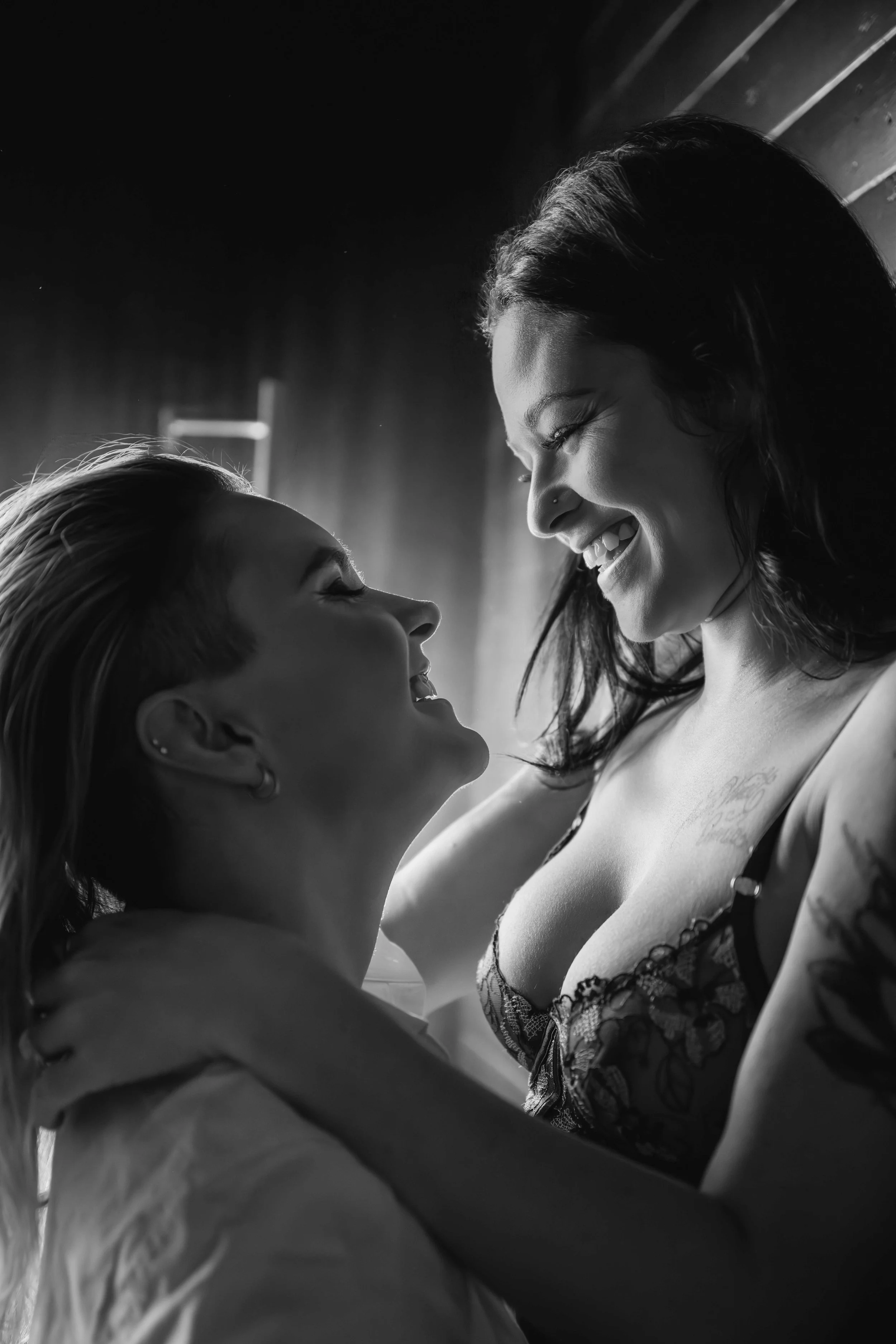Two women smiling at each other during a playful Houston couples boudoir portrait