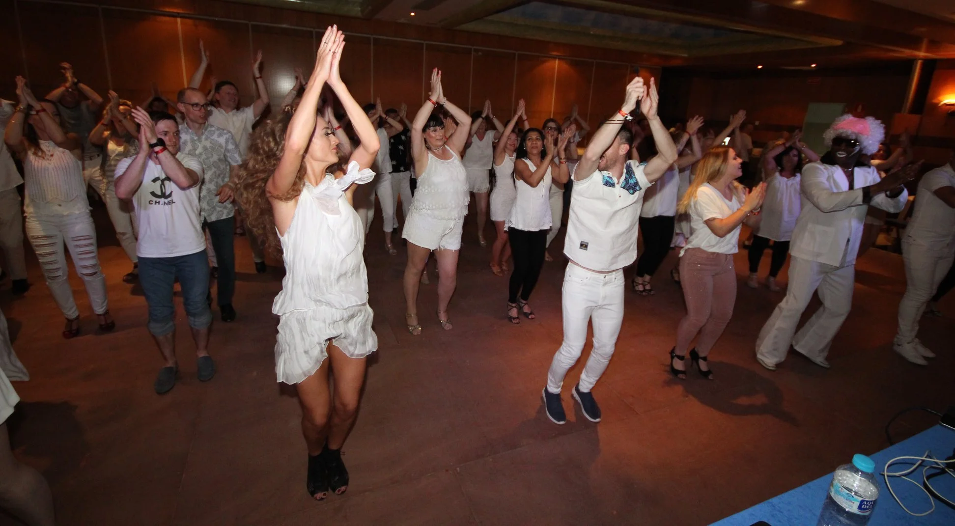 People enjoying the dancing party at a Gerry Flynn events holiday party, wearing white outfits, in a dimly lit room.