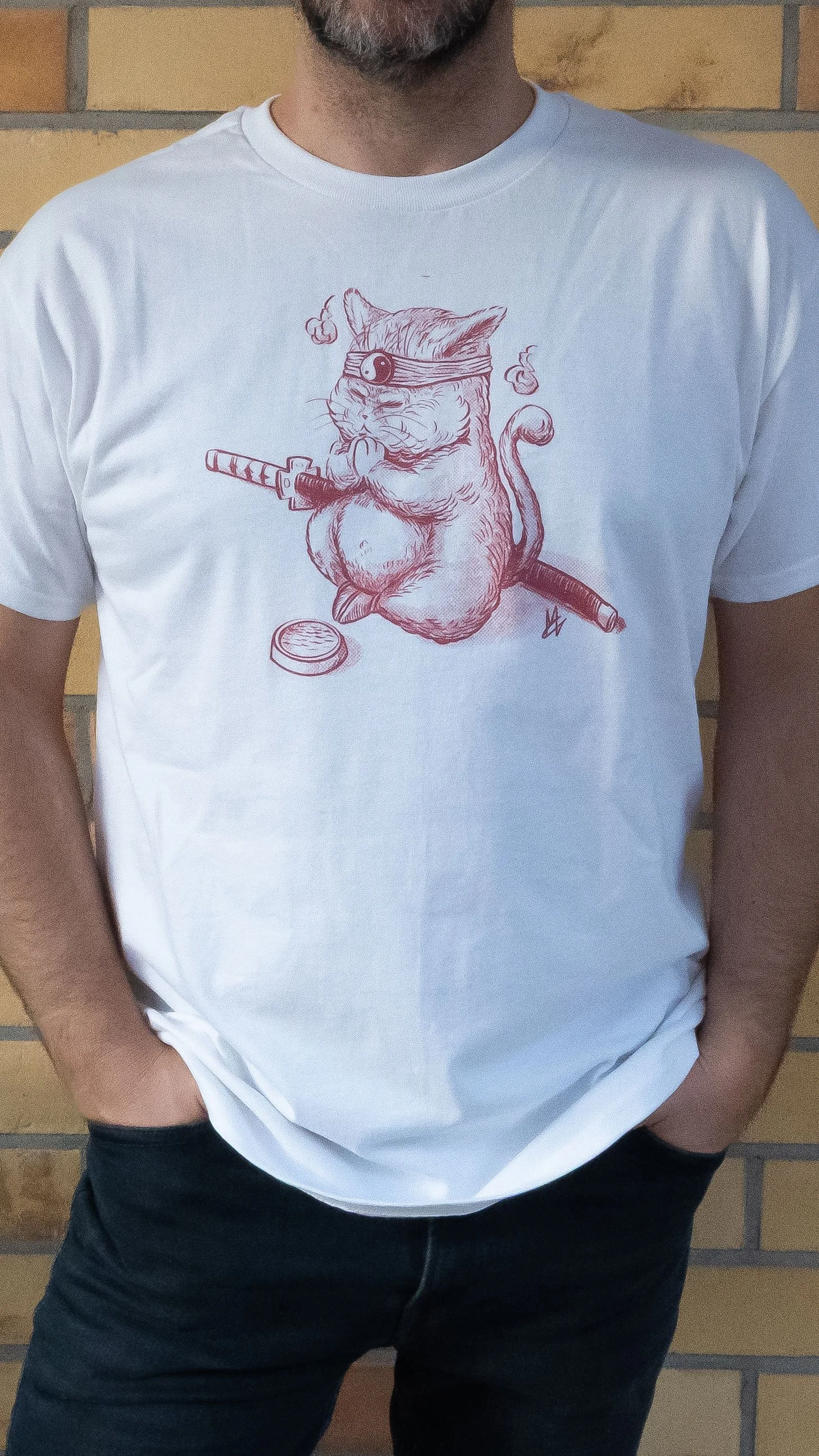 A person wearing a white T-shirt with a drawing of a cat dressed as a ninja, holding a sword in one paw, with a coin on the ground nearby.
