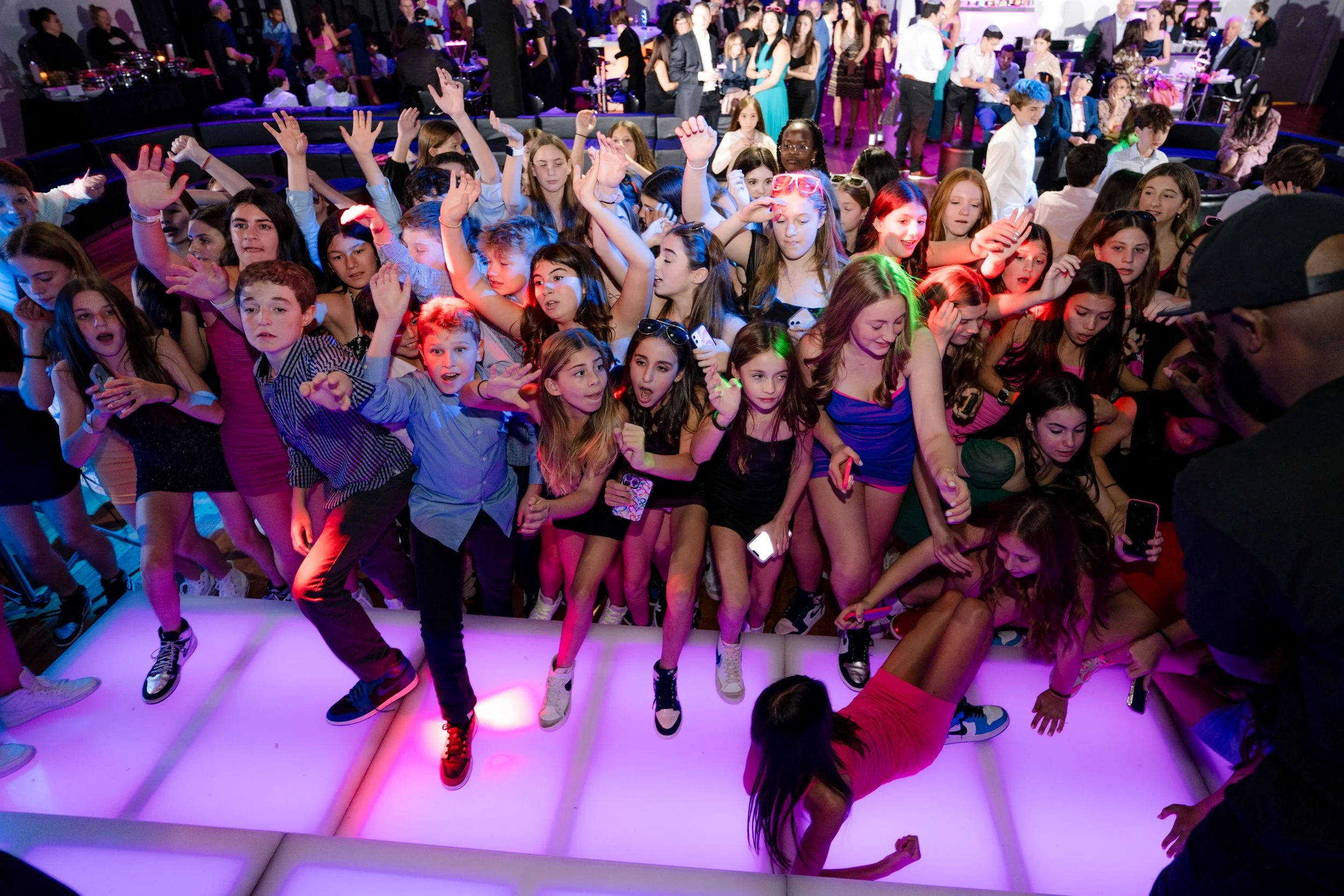 Group of young people dancing at a party on a brightly lit dance floor with colorful lighting.