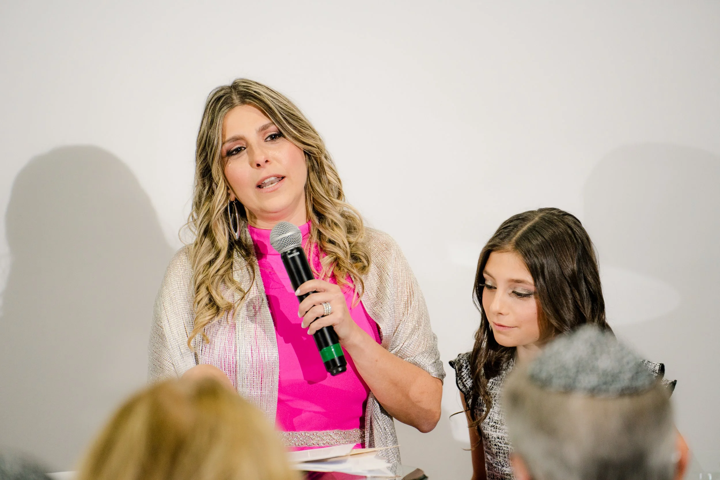 Woman speaking into a microphone next to a girl, indoors.