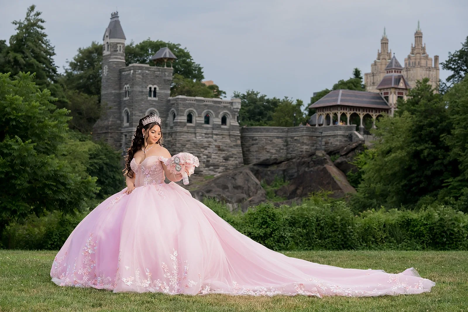 A sweet 16 girl in a pink princess-inspired quinceañera gown holding a bouquet in front of Belvedere Castle in Central Park, New York