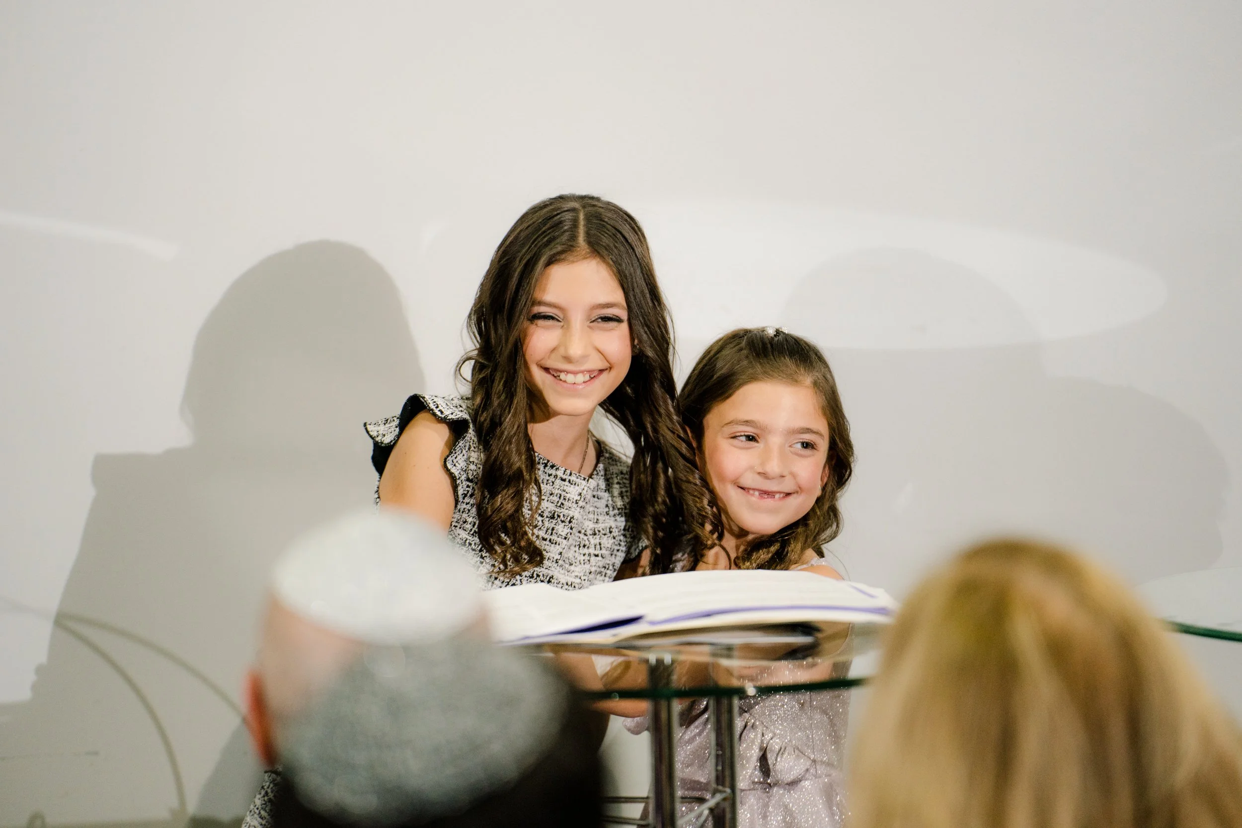 Two smiling young girls, wearing formal dresses, standing at a podium with an open book.