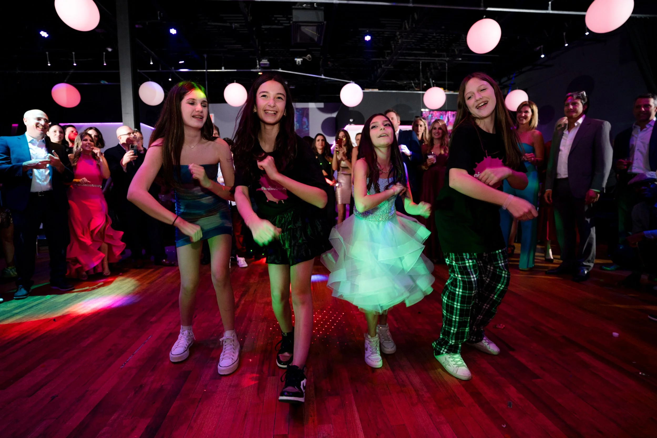 Group of children dancing at a party with an audience watching.