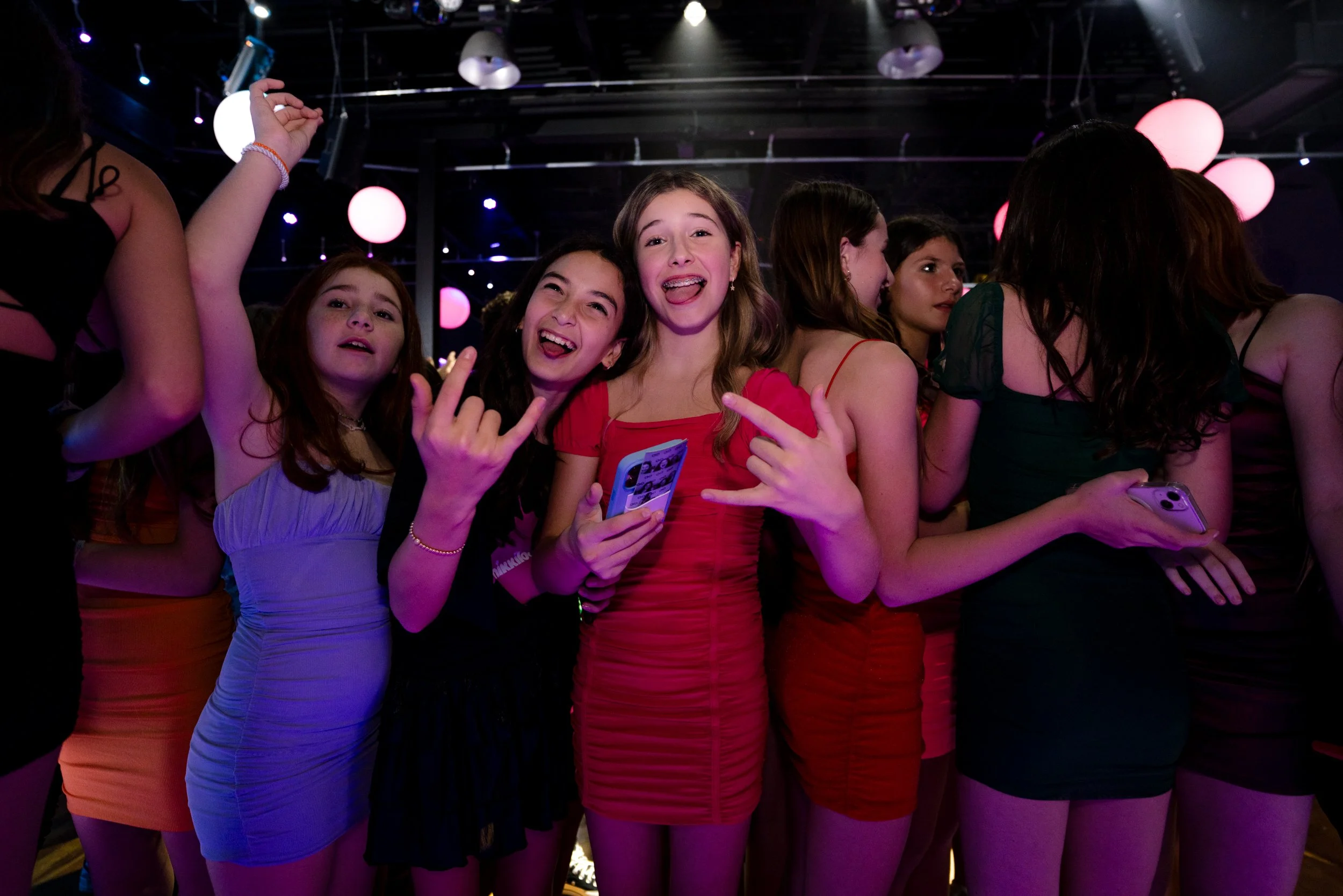 Group of young people at a party with colorful lights, posing and smiling.